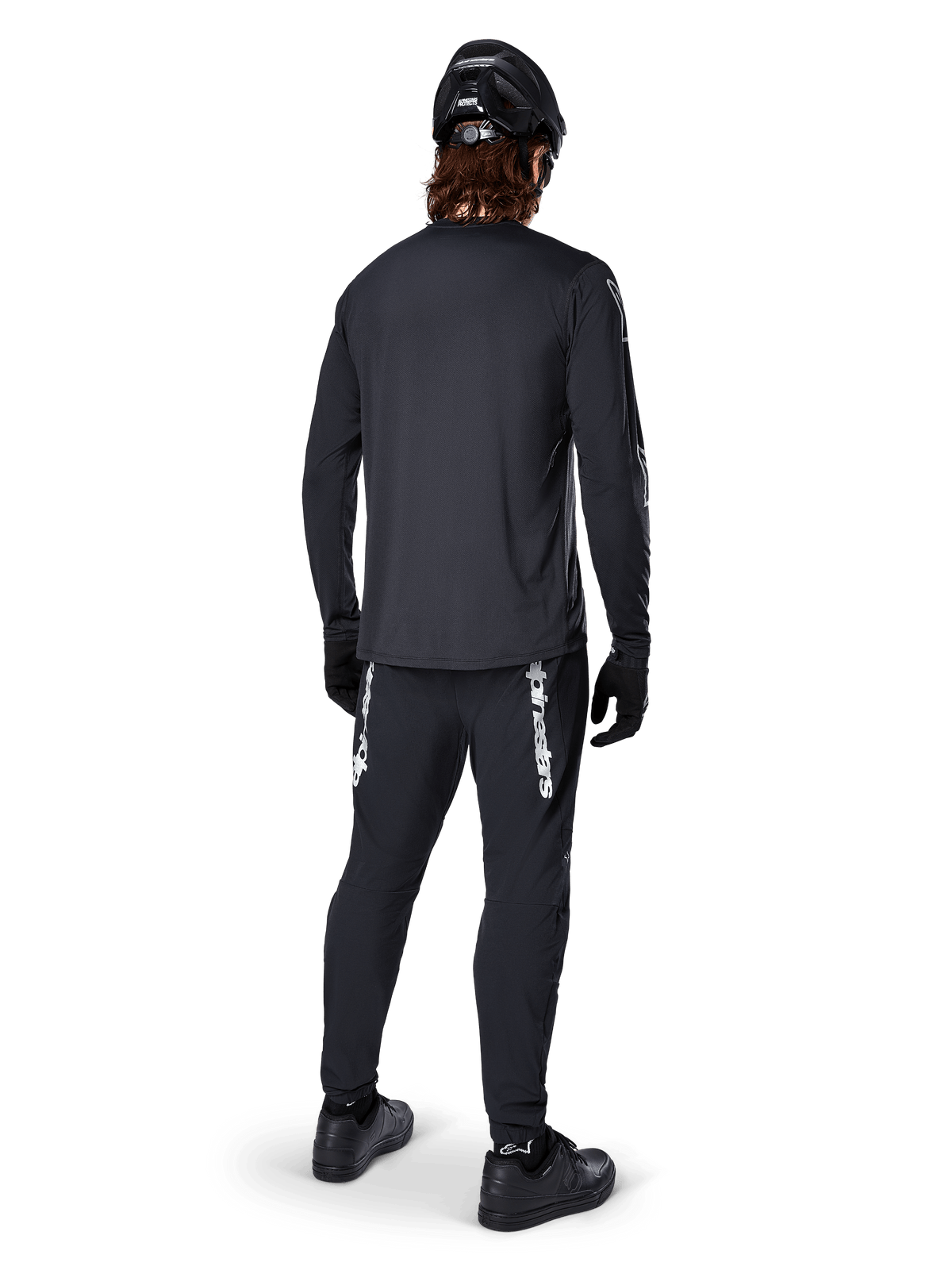 Alpinestars A-Dura Switch Long Sleeve Jersey, Black, rear view on a rider, worn with black pants featuring white Alpinestars branding, black helmet, and gloves, featuring a drop tail for extra coverage, performance mountain bike apparel