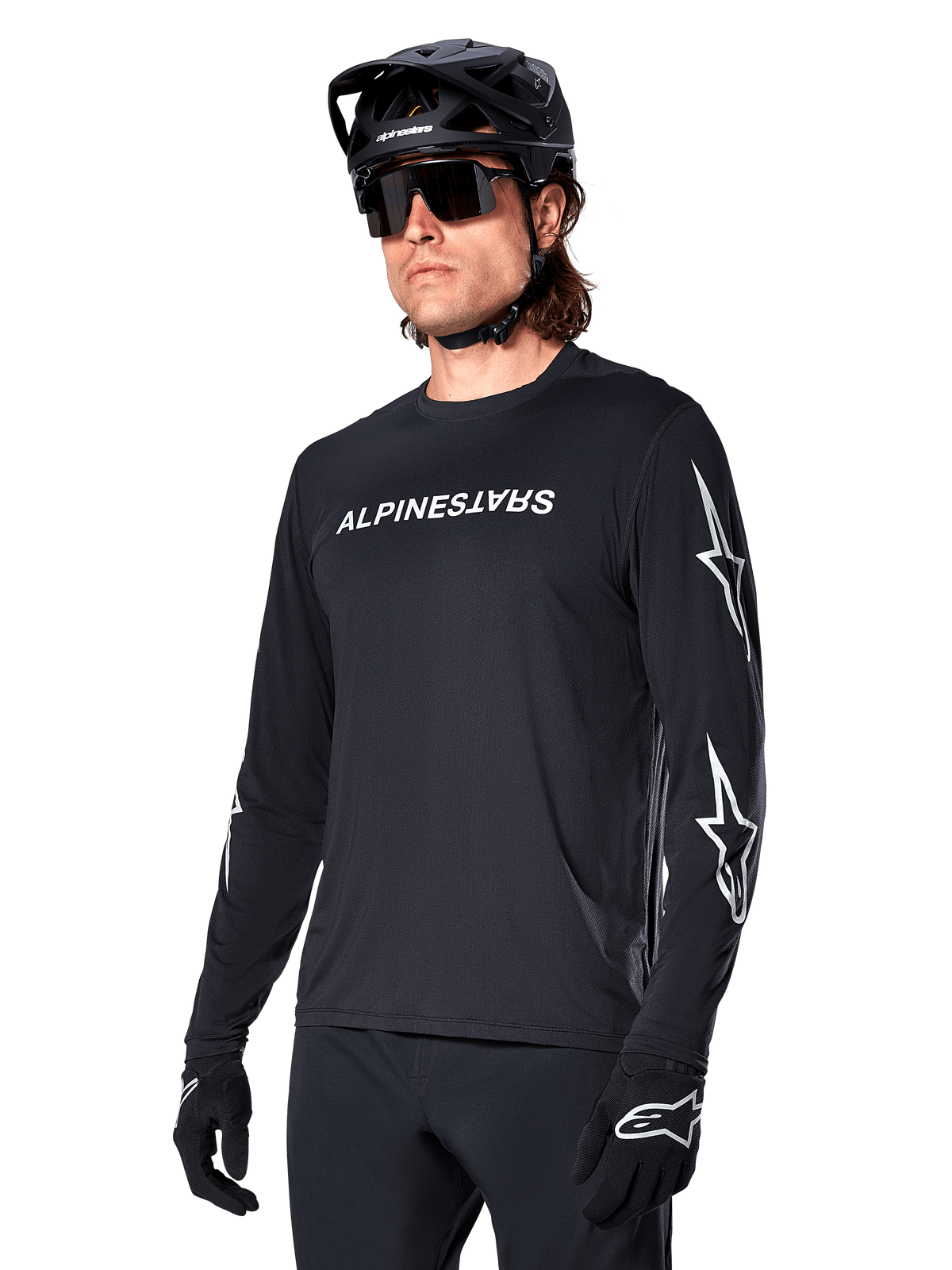 Male cyclist wearing Alpinestars A-Dura Switch Long Sleeve Jersey, Black with white wordmark and star logos on sleeves, styled with black MTB helmet and sunglasses, high-performance cycling gear for off-road riding