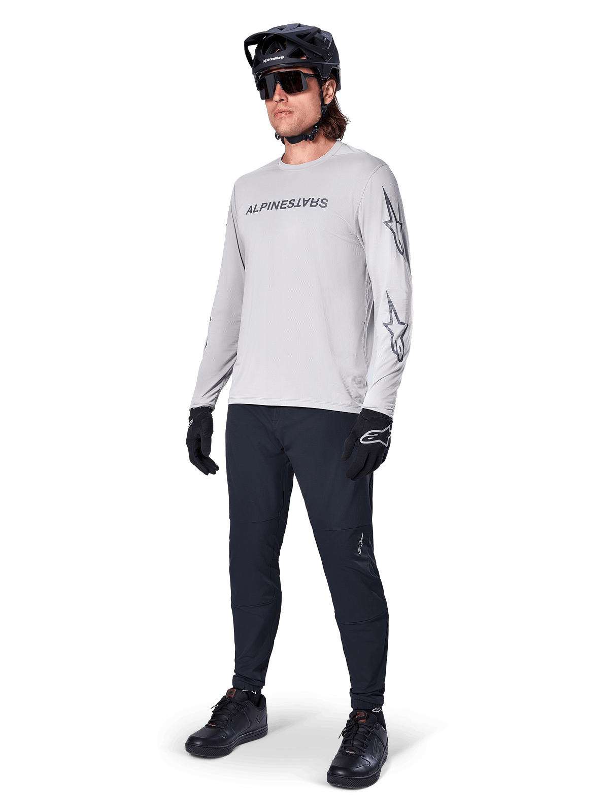 Alpinestars A-Dura Switch Langarmtrikot, Hellgrau, getragen von männlichem Fahrer mit schwarzer Mountainbike-Hose und Helm, schwarzes Wortmarken-Logo auf der Brust und Sterngrafiken auf den Ärmeln, Performance-Offroad-Radsportbekleidung