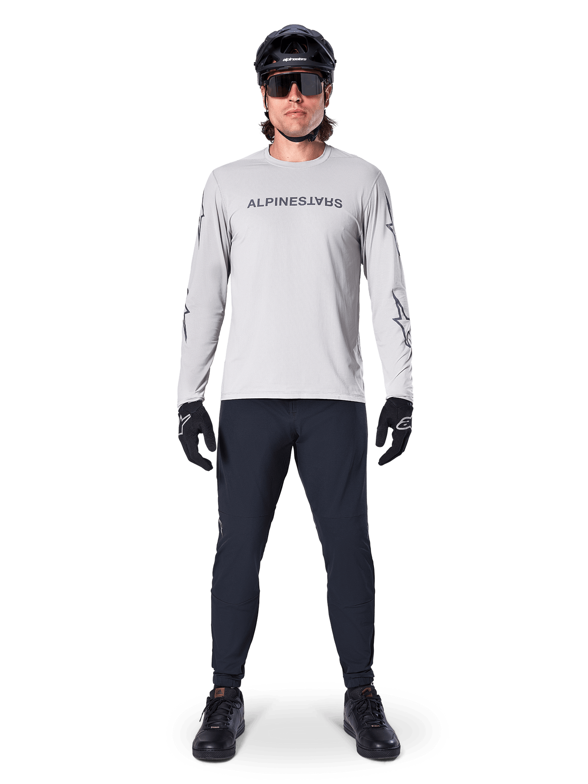 Alpinestars A-Dura Switch Langarmtrikot in Hellgrau, mit stilisiertem Wortmarken-Logo auf der Brust, getragen mit schwarzer Hose, Helm und Handschuhen, Performance-Mountainbike-Bekleidung für das Geländeradfahren