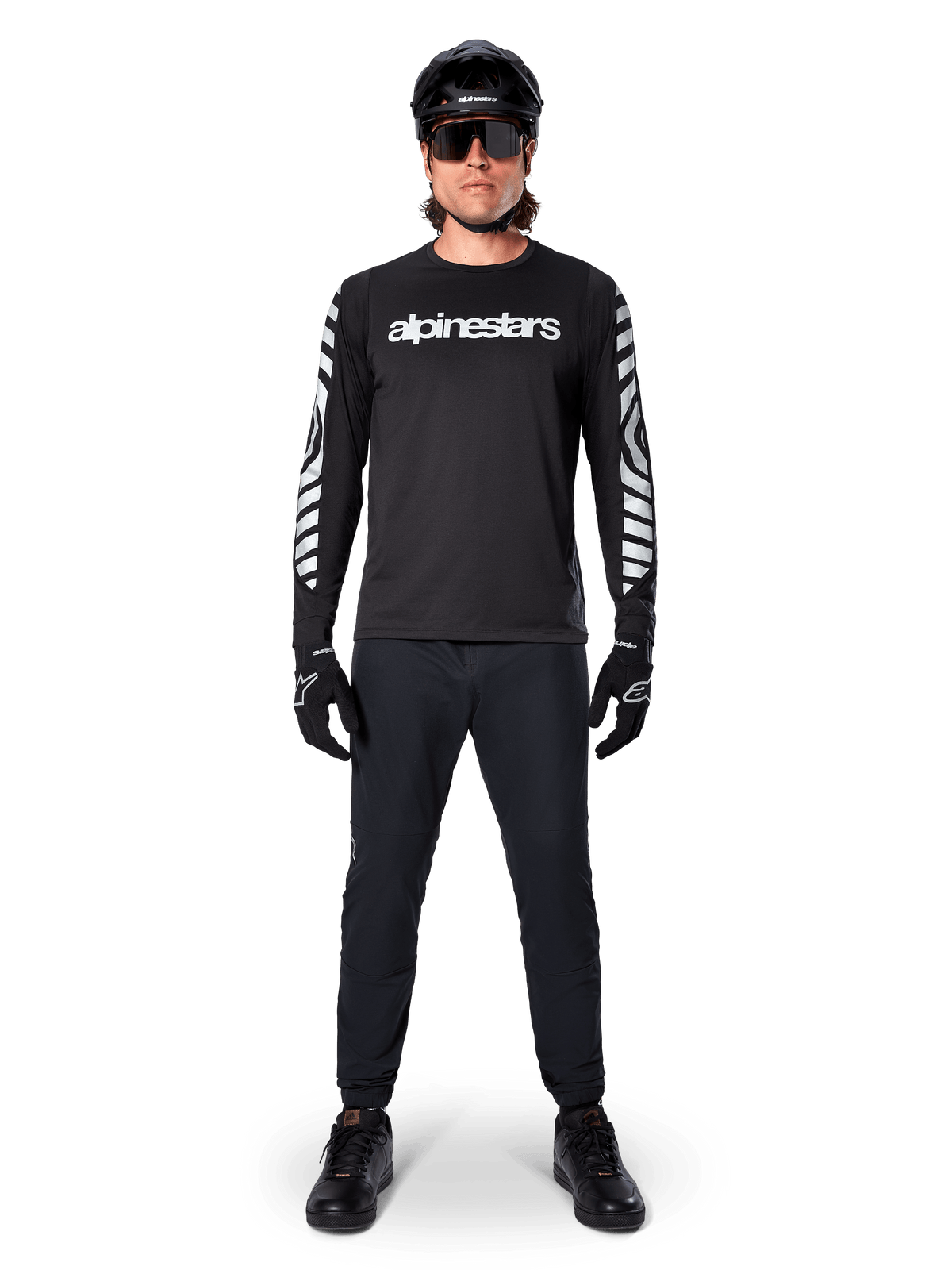Alpinestars A-Dura Dri Oscar Langarmtrikot in Black Reflective, getragen mit schwarzem Helm und Sonnenbrille, mit weißem Brustlogo und reflektierenden Grafikmustern an den Ärmeln, MTB-Ausrüstung für Offroad-Fahrten