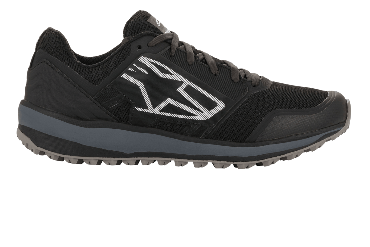 Alpinestars Meta Trail Schuhe, Performance-Laufschuhe, Schwarz und Dunkelgrau, Seitenansicht mit großem weißen geometrischen Astars-Logo, Mesh-Obermaterial mit grauer Zwischensohle und profilierter Gummisohle, lässiges Motorsport-Paddock-Schuhwerk