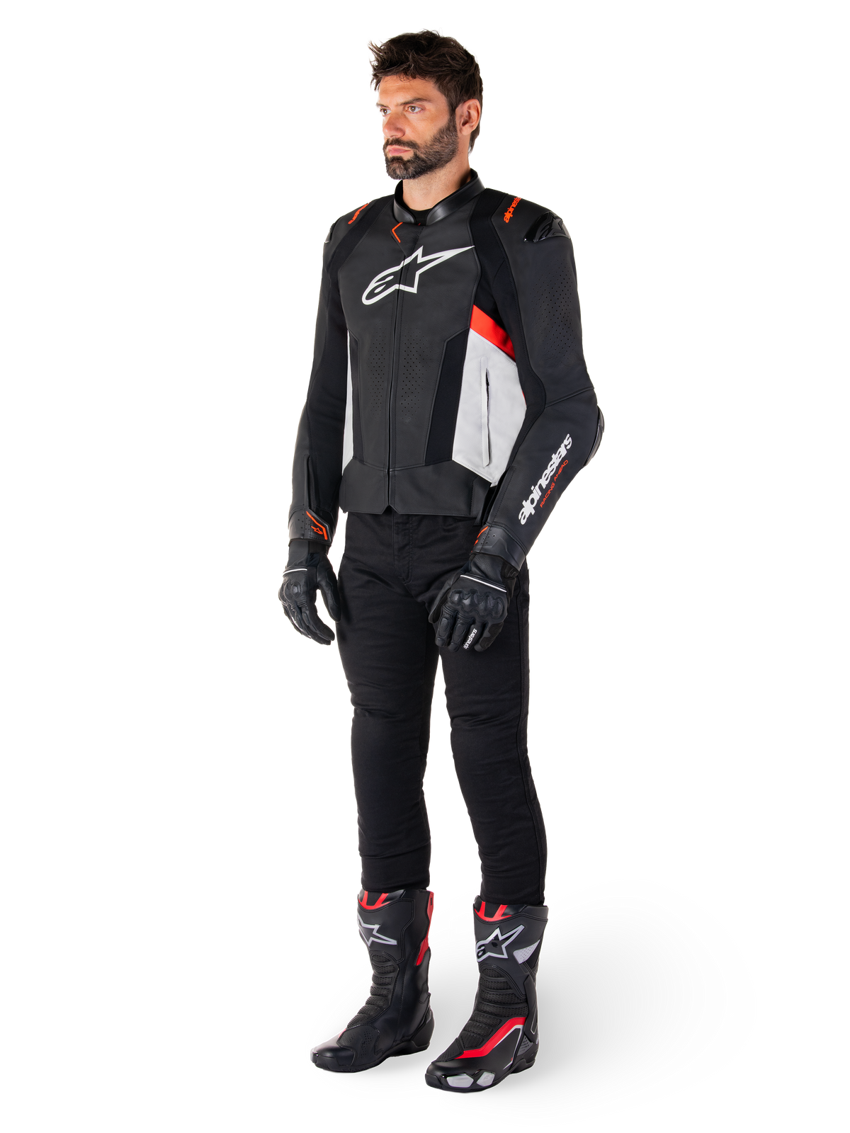 Männliches Model in der Alpinestars Missile V3 Lederjacke in Schwarz, Weiß und Fluo-Rot, kombiniert mit schwarzer Motorradhose, Handschuhen und Stiefeln, hochwertige Rindslederkonstruktion mit markantem Alpinestars-Branding, professionelle Rennsport-Ästhetik