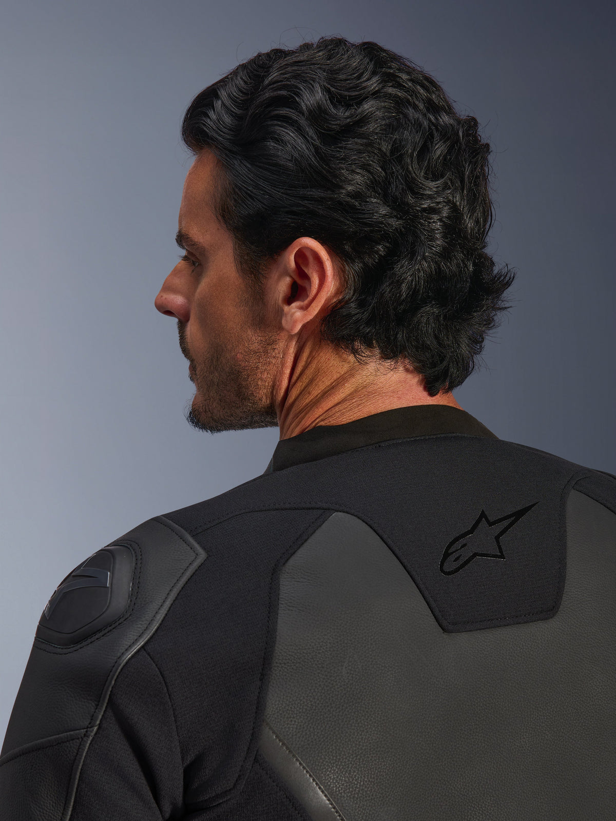 Alpinestars GP Force V2 Lederjacke, Schwarz, Nahaufnahme von hinten, mit dem schwarzen Stern-Logo am oberen Rücken und GP Lite Evo DFS Schulterprotektor, Mehrpanel-Konstruktion aus Leder und Textil, Studioansicht des Fahrerprofils und der Ausrüstungsdetails.