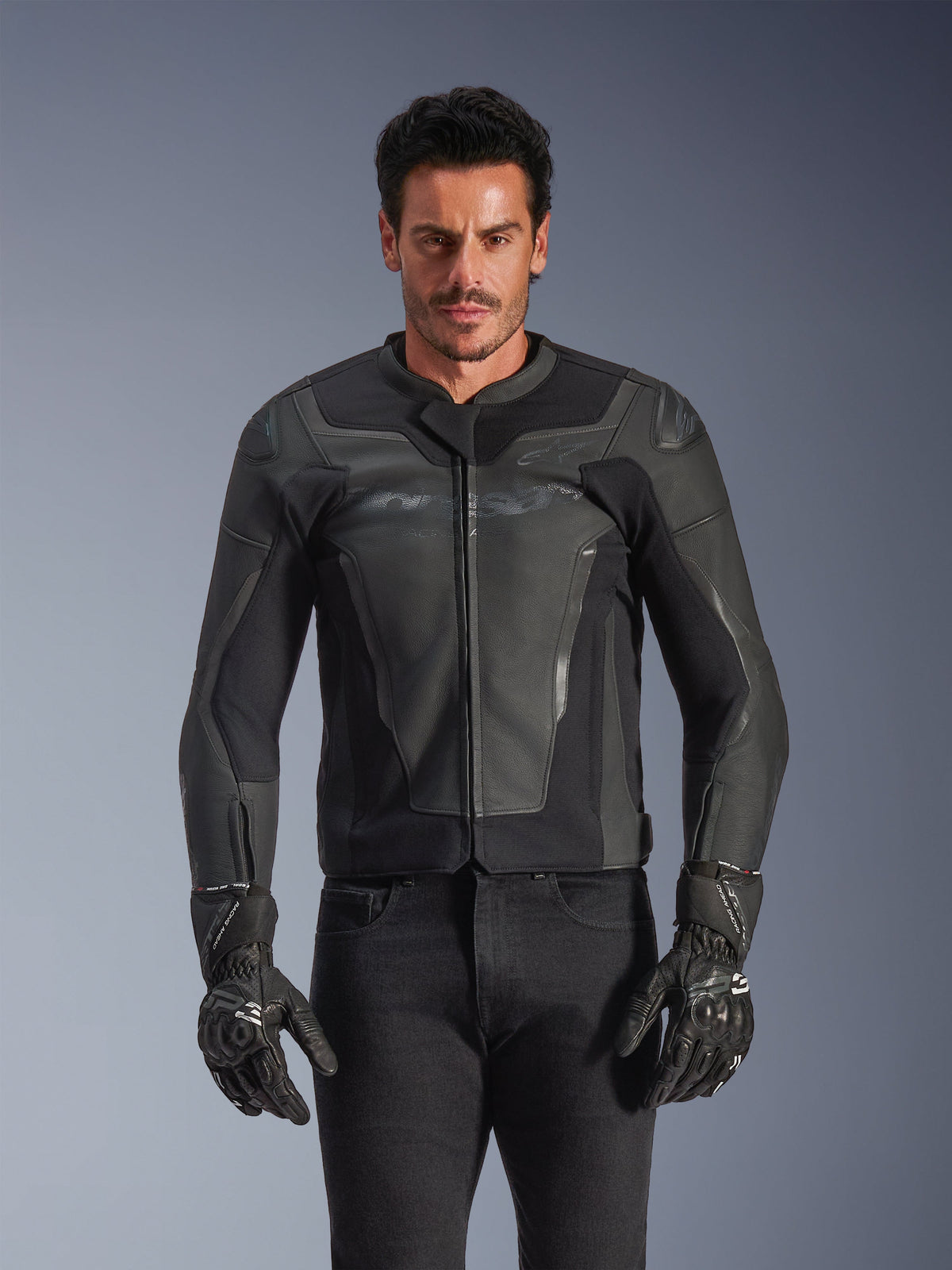 Alpinestars GP Force V2 Lederjacke, Schwarz und Dunkelgrau, Motorrad-Rennjacke, Mann in elegantem, körperbetontem Lederdesign mit Frontreißverschluss, kombiniert mit schwarzen strukturierten Handschuhen, moderne Schutzausrüstung, erstklassige Lederkonstruktion