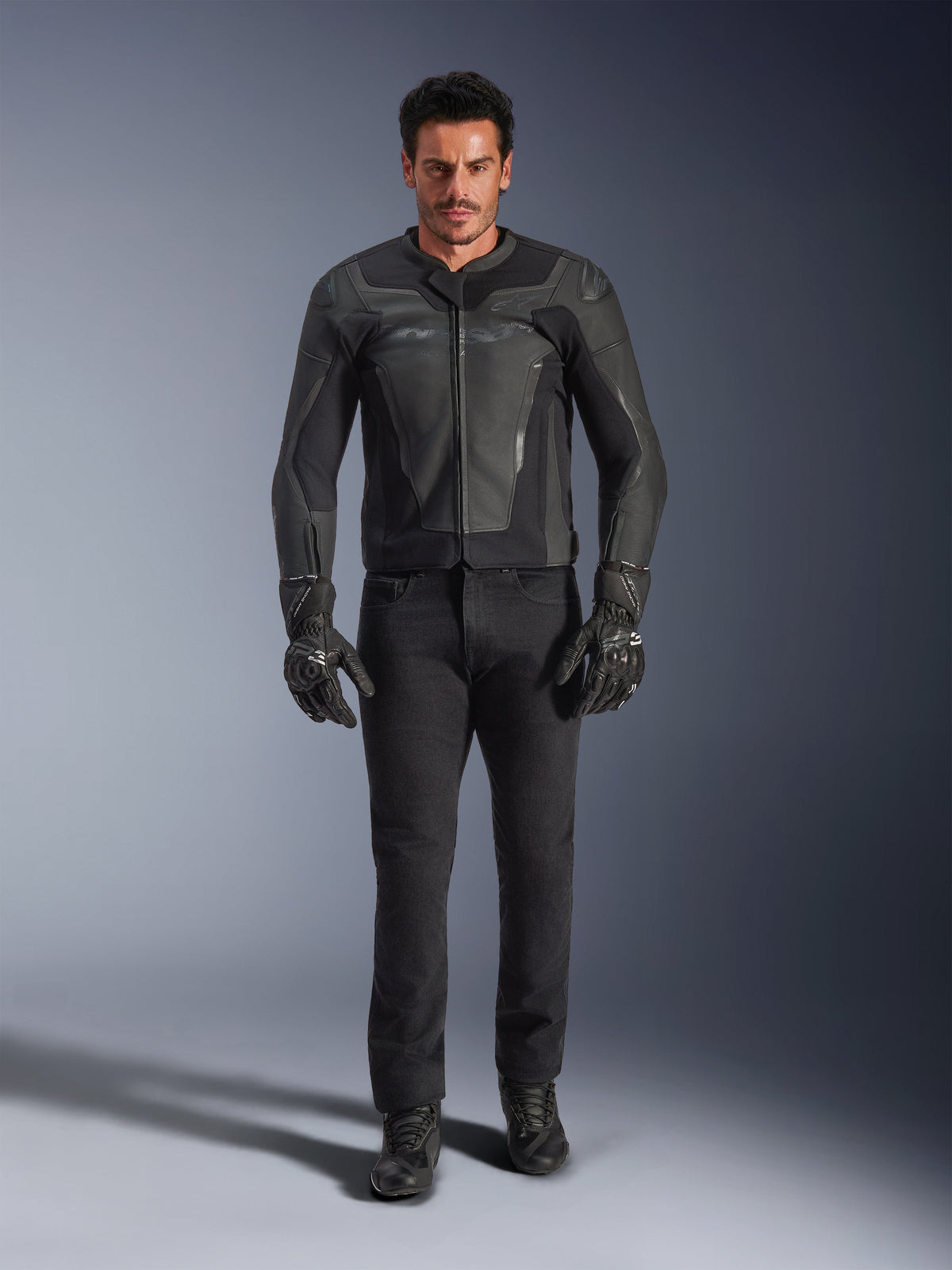 Alpinestars GP Force V2 Lederjacke in Schwarz, getragen von einem männlichen Fahrer mit schwarzer Motorradhose, Handschuhen und Stiefeln, schlanke Lederkonstruktion im Sport-Stil mit Schulterschleifern und integriertem Schutz