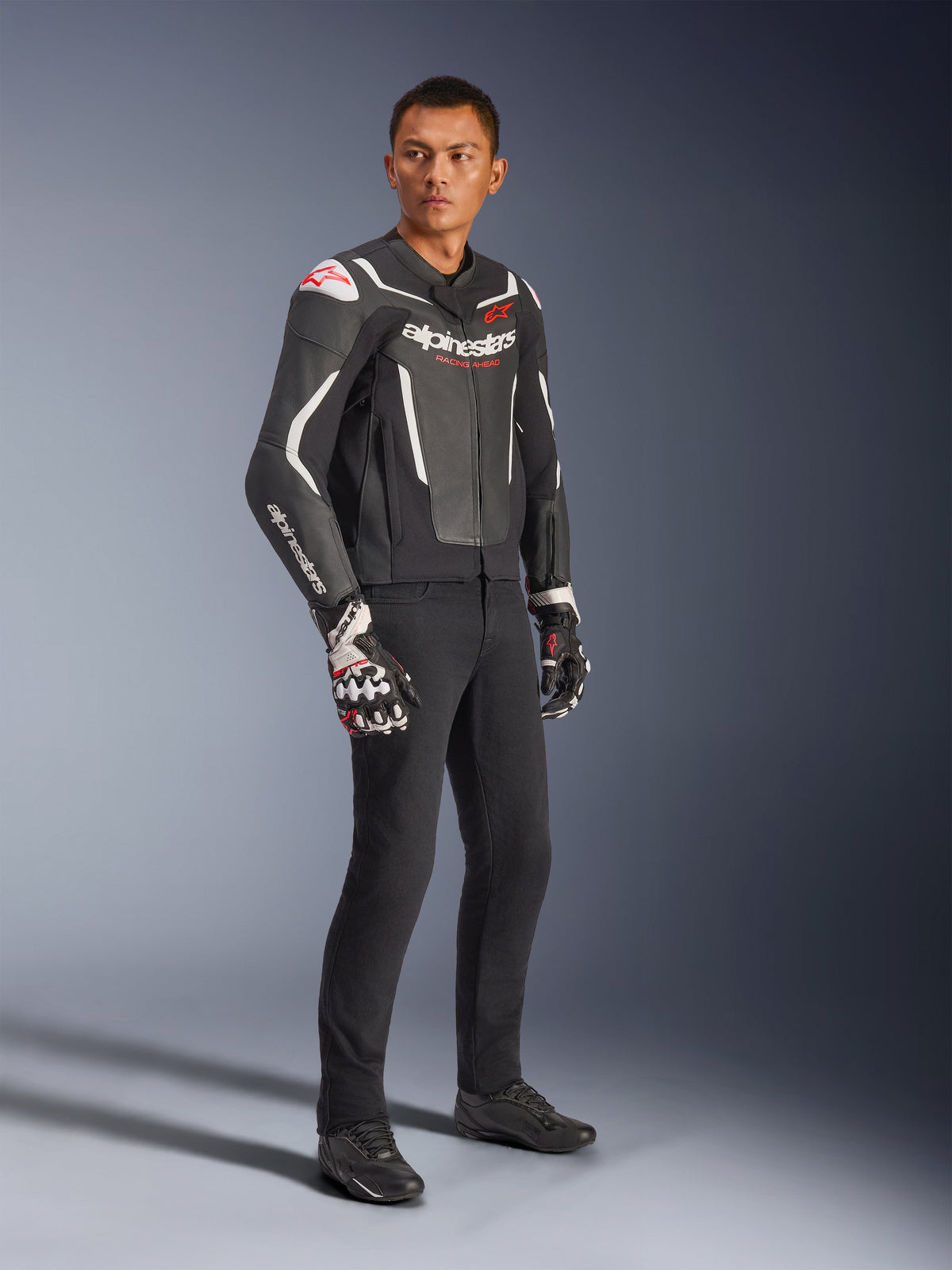 Alpinestars GP Force V2 Lederjacke, Schwarz und Weiß, getragen von einem männlichen Model mit schwarzer Motorradhose und technischen Handschuhen, mit roten Alpinestars-Logos, sportlich geschnittene Leder-Motorradjacke für Straßenfahrten