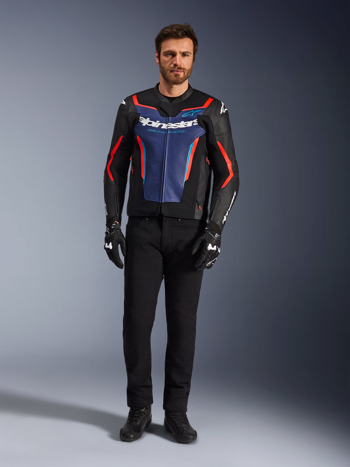 Alpinestars GP Force V2 Lederjacke, Schwarz, Blau und Fluo-Rot, getragen von einem männlichen Model mit schwarzer Hose und Motorradhandschuhen, Sport-Motorradjacke aus Rindsleder mit rennsportinspiriertem Design, Vorderansicht
