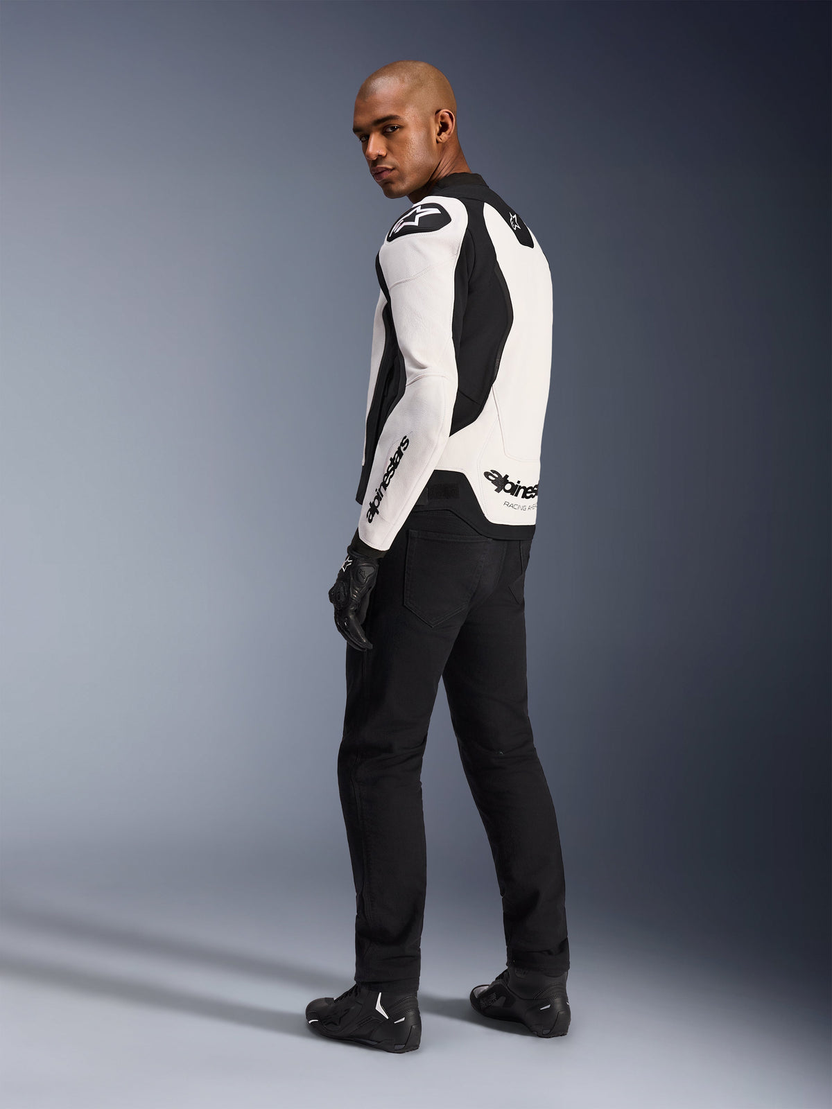 Alpinestars GP Force V2 Leather Jacket, White and Black, back profile view worn by a model, featuring white bovine leather with black stretch panels, Alpinestars logos on the shoulder and back, paired with black riding pants and boots.