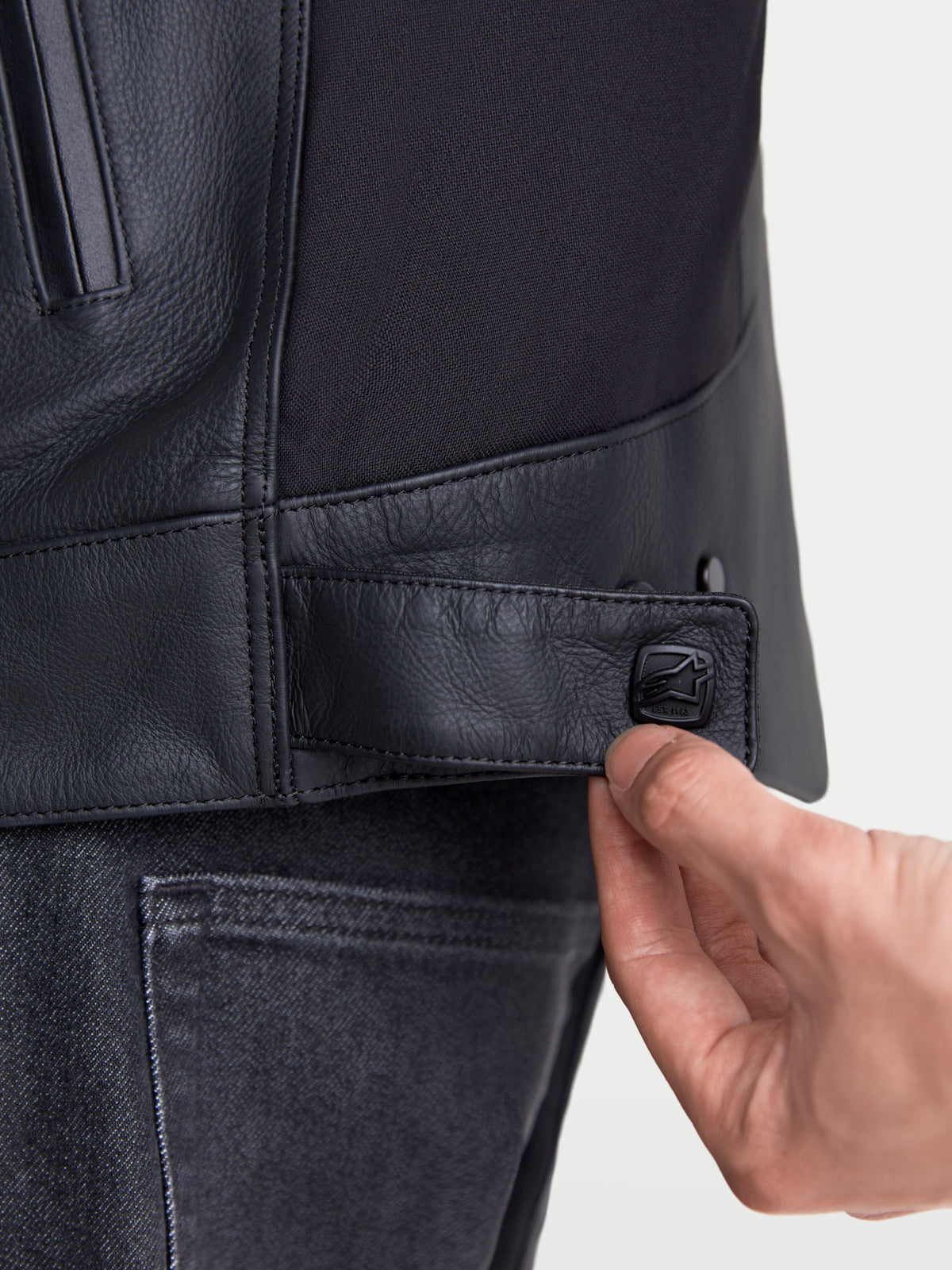 Alpinestars Maver-X Leather Jacket, men's urban motorcycle leather jacket, close-up view of the adjustable snap fastening tab at the waist in black, premium leather and stretch insert construction