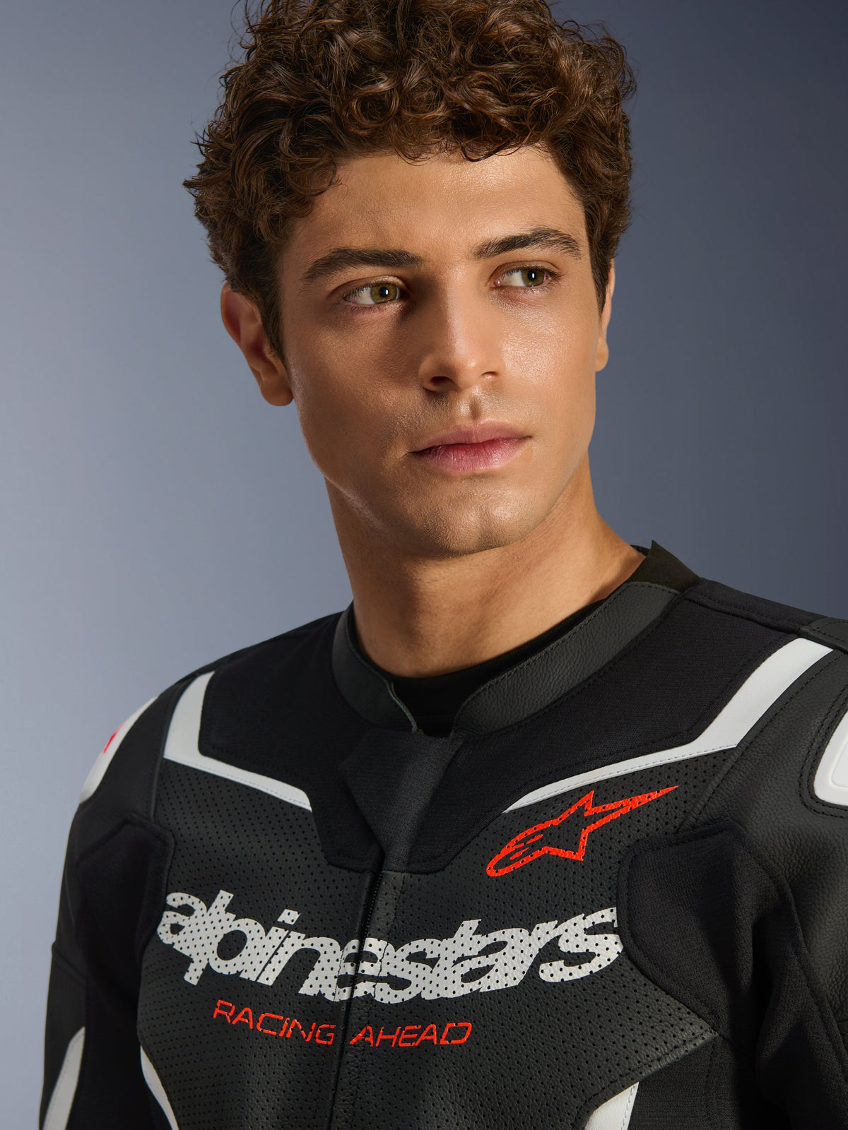 Porträt eines männlichen Models in der Alpinestars GP Force V2 Air Lederjacke in Schwarz und Weiß, mit perforierter Lederkonstruktion, markantem weißem Logo und rotem 'RACING AHEAD'-Schriftzug auf der Brust, Sport-Motorradbekleidung