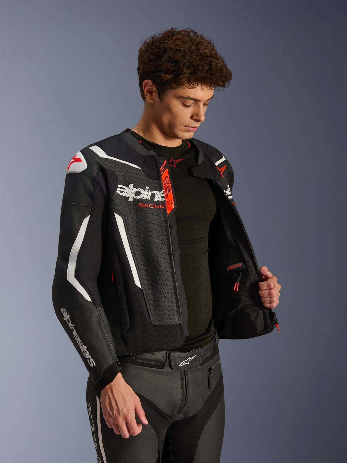 Alpinestars GP Force V2 Air Lederjacke, Schwarz und Weiß mit roten Akzenten, perforierte Lederkonstruktion, geöffnet, um die Innenseite und die schwarze Basisschicht zu zeigen, kombiniert mit passender Lederhose, professionelle Studioaufnahme für Motorrad-Straßenausrüstung