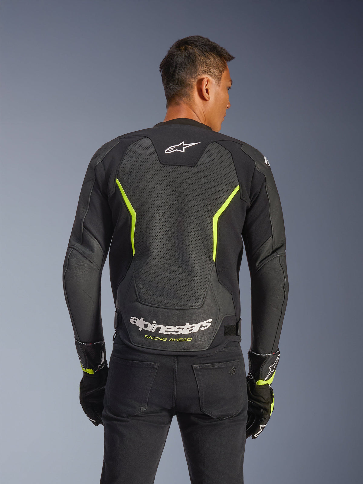 Alpinestars GP Force V2 Air Lederjacke, Schwarz und Gelb Fluo, Rückansicht eines männlichen Fahrers mit großflächig perforierten Lederbahnen für optimale Belüftung, weißes Alpinestars-Branding und gelber „Racing Ahead“-Schriftzug am unteren Rücken, Sport-Motorradausrüstung für die Straße.