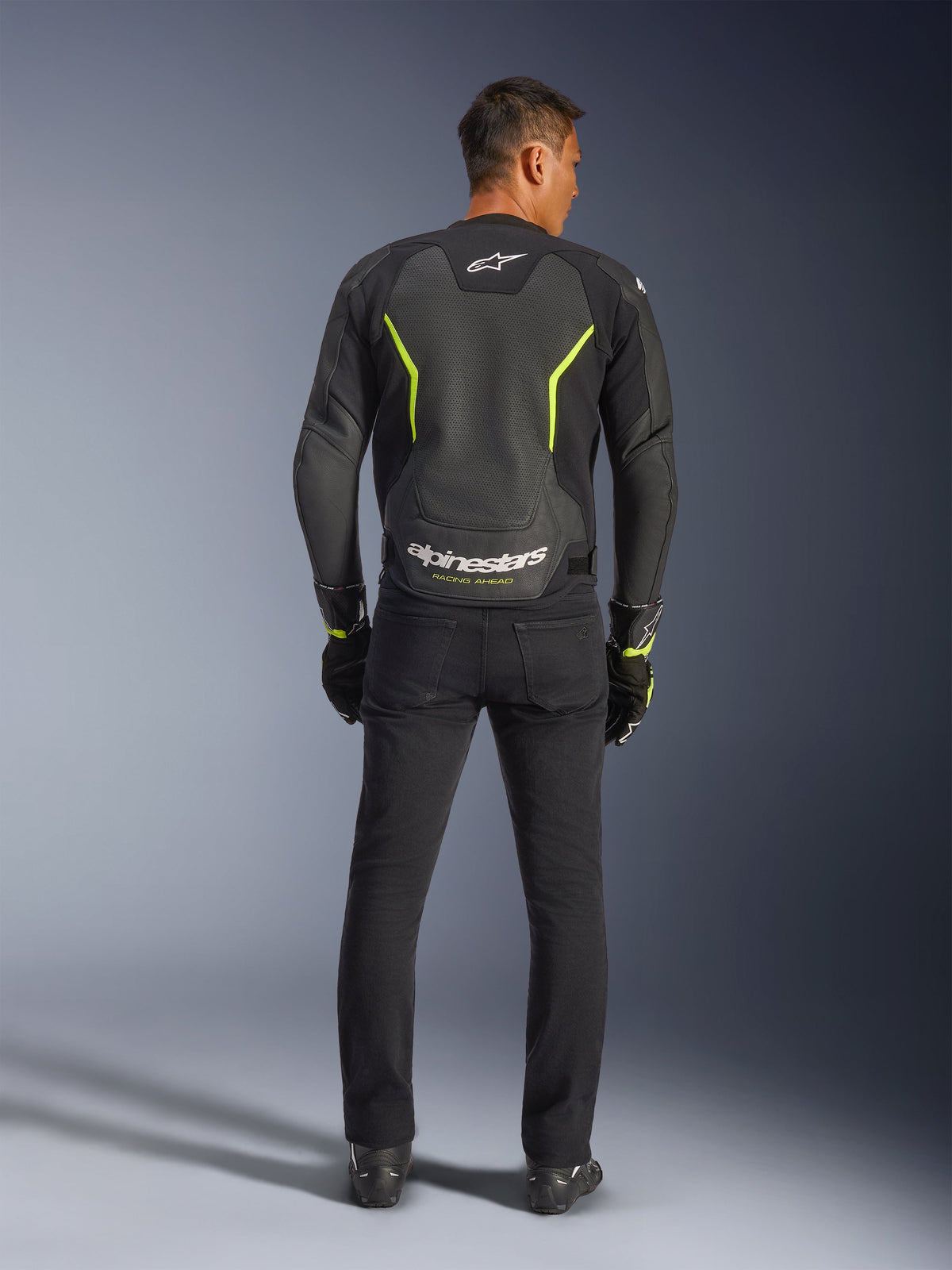 Alpinestars GP Force V2 Air Lederjacke, Schwarz und Gelb Fluo, Rückansicht eines Modells in der Sport-Motorradjacke, mit großen perforierten Bereichen, neongelben Akzenten und weißem 'alpinestars'-Branding am unteren Rücken, kombiniert mit schwarzer Fahrausrüstung