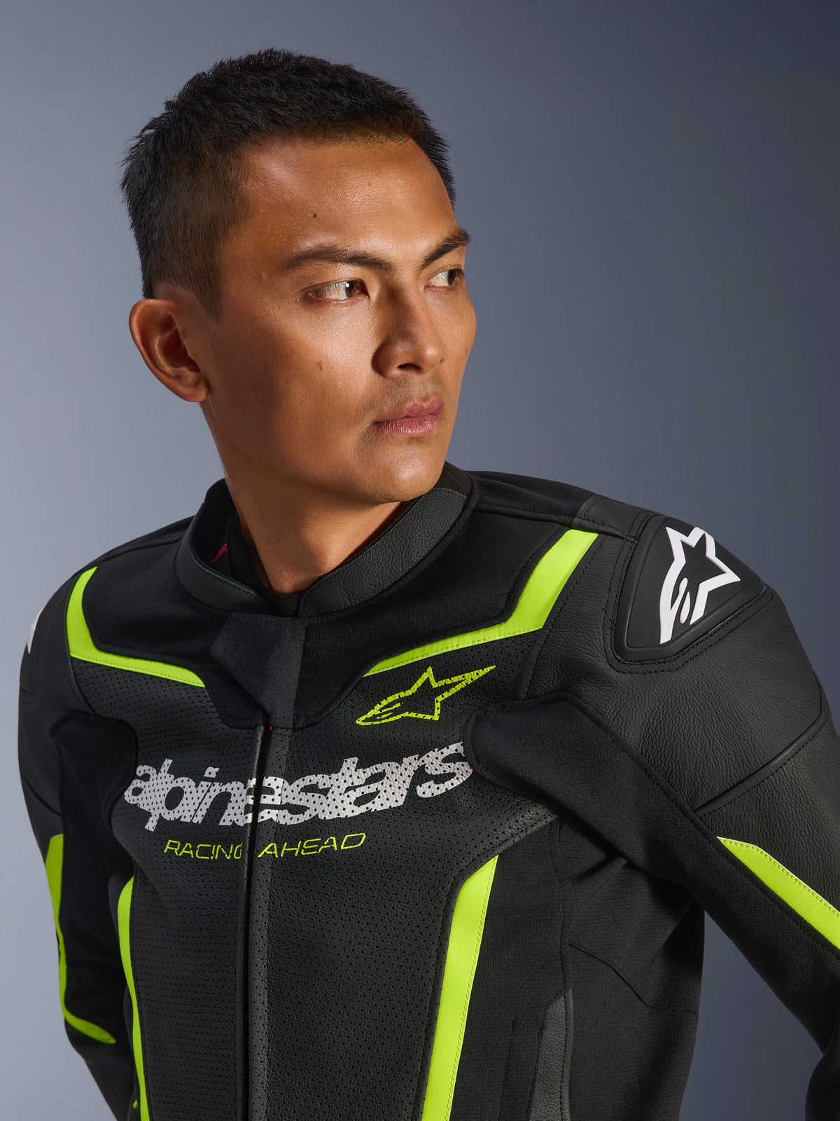 Alpinestars GP Force V2 Air Lederjacke, Schwarz und Gelb Fluo, perforierte Sport-Motorradjacke mit weißem Brustlogo und „Racing Ahead“-Schriftzug, neonfarbenen Akzenten und schützenden Schulterslidern, getragen von einem männlichen Model.