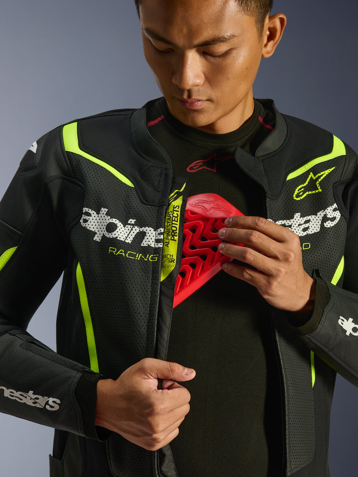 Alpinestars GP Force V2 Air Lederjacke, Schwarz und Gelb Fluo, perforierte Motorradlederjacke, getragen von einem Fahrer, der das Brustfach mit einem roten Protektoreinsatz zeigt, weißes Alpinestars-Branding, umfangreiche Airflow-Perforationen.