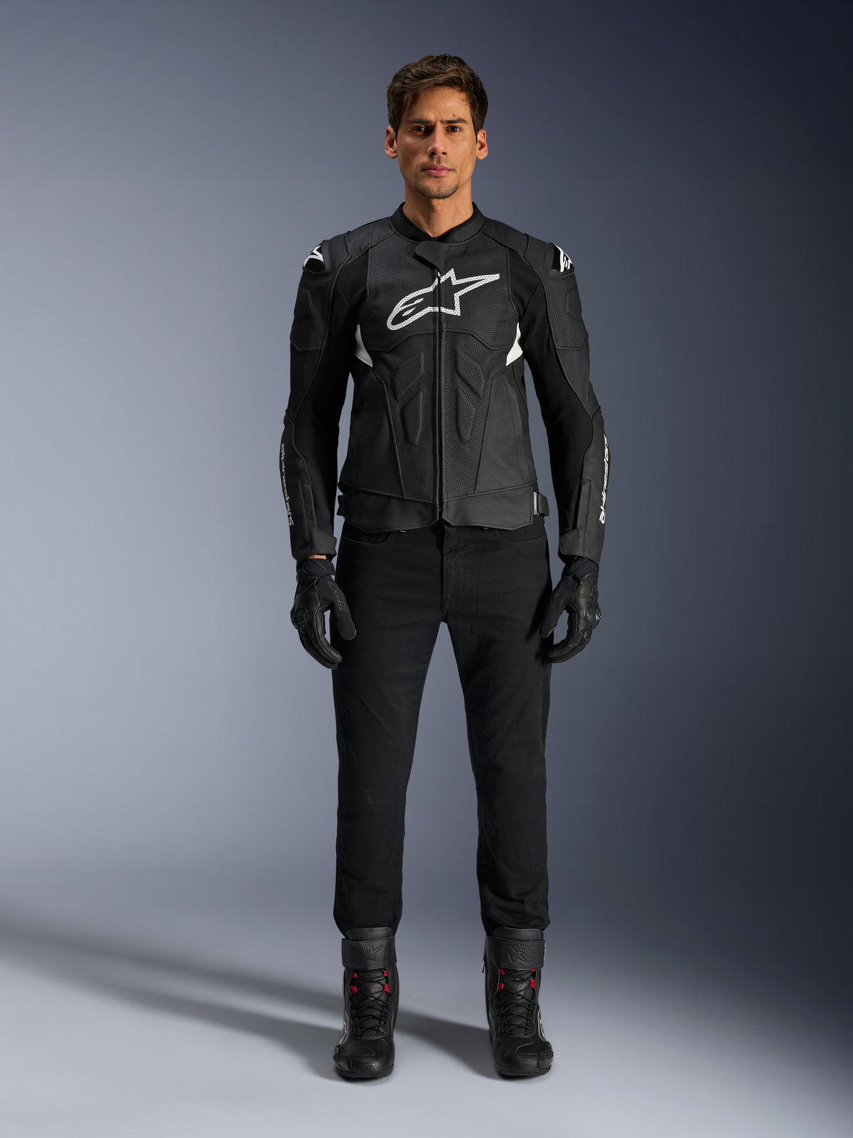 Alpinestars Dusk Airflow Lederjacke, Schwarz und Weiß, Motorrad-Lederjacke mit perforierten Paneelen für Luftzirkulation, weißes Astars-Logo auf der Brust, getragen von einem männlichen Fahrer mit schwarzer Hose, Handschuhen und Motorradstiefeln, professionelle Studioaufnahme für Sport-Motorradbekleidung.