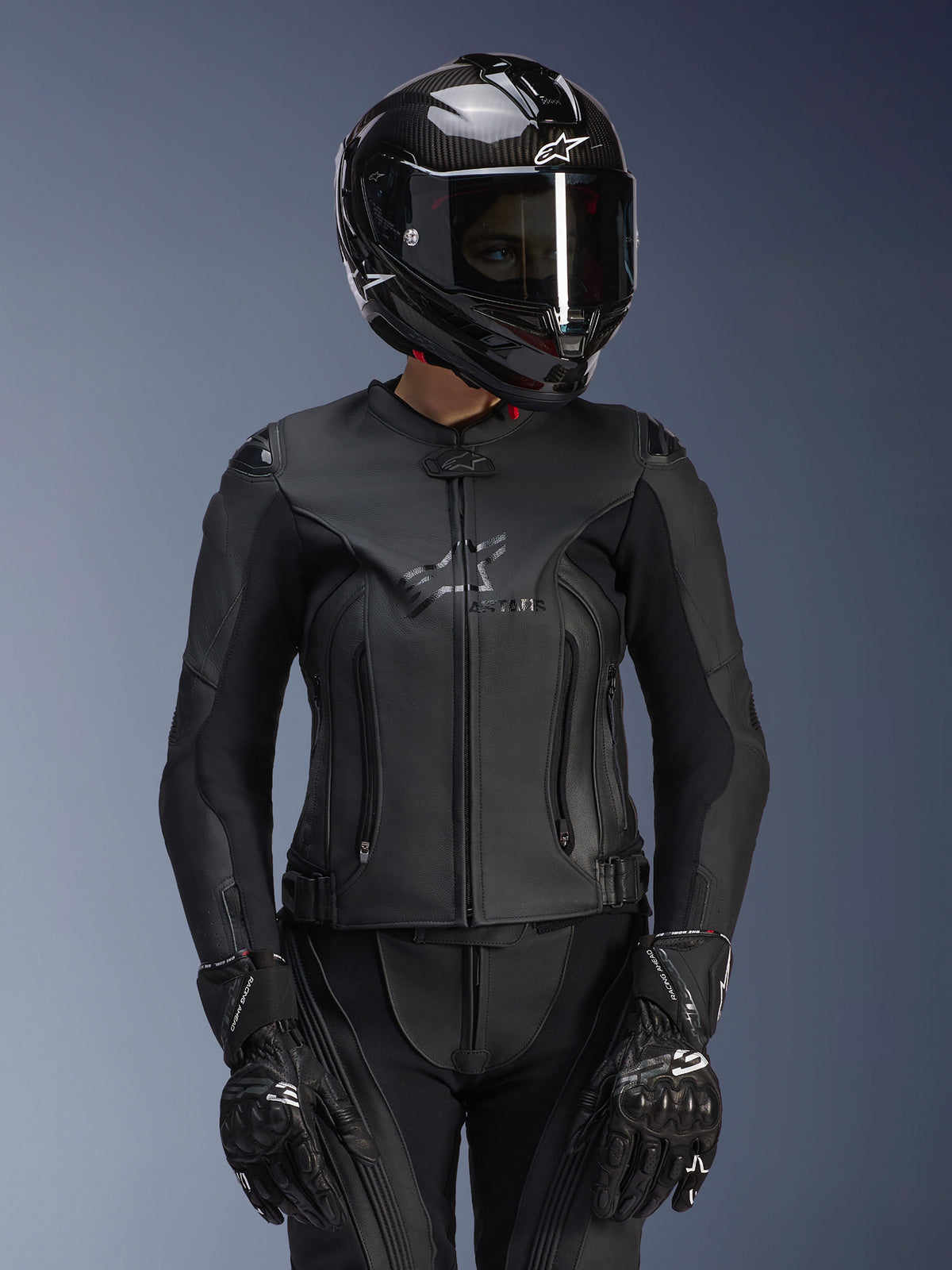 Alpinestars Women Stella GP Plus V4 Leather Jacket in Black Black, worn with a black carbon fiber helmet and racing gloves, sleek leather construction with subtle chest branding, tailored silhouette for female riders, professional sport motorcycle gear