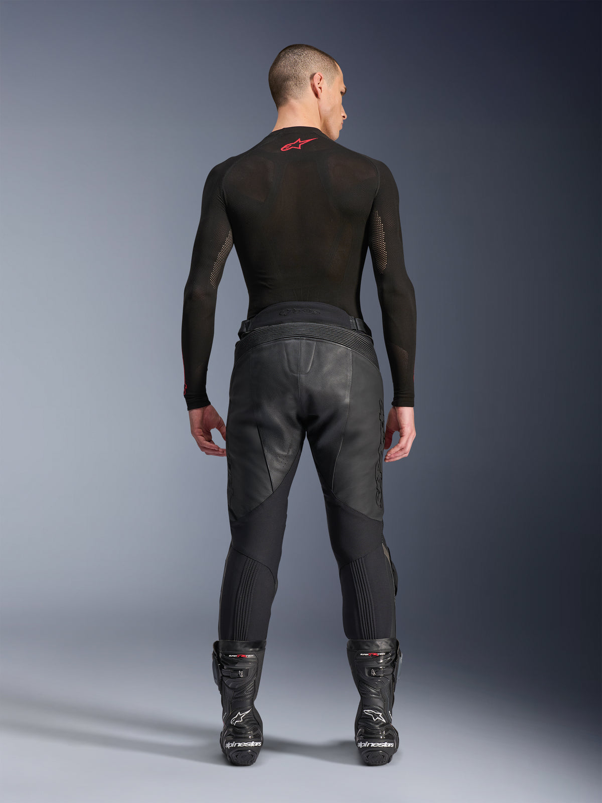 Alpinestars Missile V3 Lederhose, Schwarz, Rückansicht an einem Model mit schwarzem langärmeligem Kompressionsshirt und Rennstiefeln, hochwertige Lederkonstruktion mit hoher Taille und Stretchzonen, professionelle Motorrad-Rennausrüstung