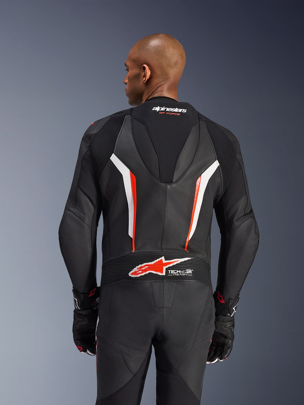 Alpinestars GP Force V2 Lederkombi, 1-teiliger Motorradanzug, Schwarz, Weiß und Fluo-Rot, Rückansicht des Oberkörpers zeigt perforiertes Leder und Tech-Air Ready-Logo, getragen mit passenden schwarz-roten Handschuhen