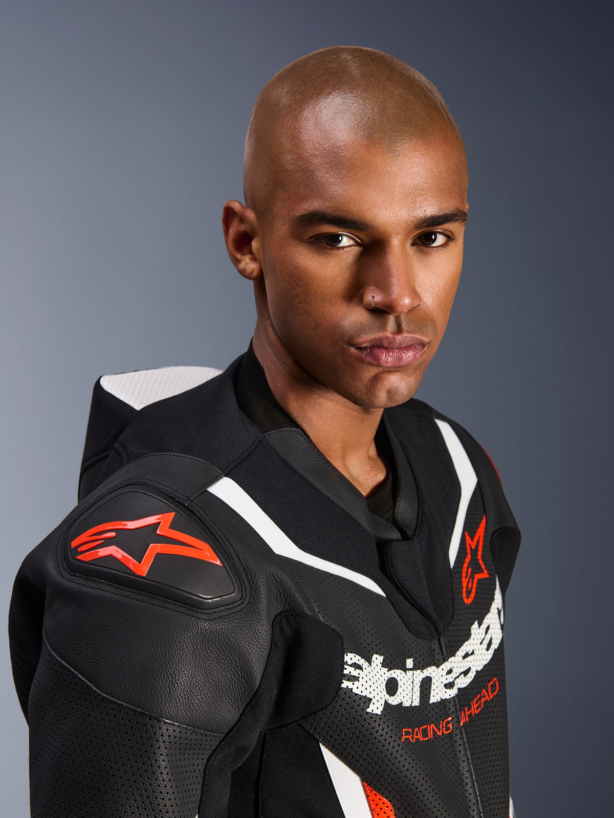 Nahaufnahme eines Models im Alpinestars GP Force V2 Lederkombi, 1-teilig, Schwarz, Weiß und Fluo-Rot, mit perforierten Ledereinsätzen, weißen Rennstreifen und roten Alpinestars-Logos auf Schulter und Brust.