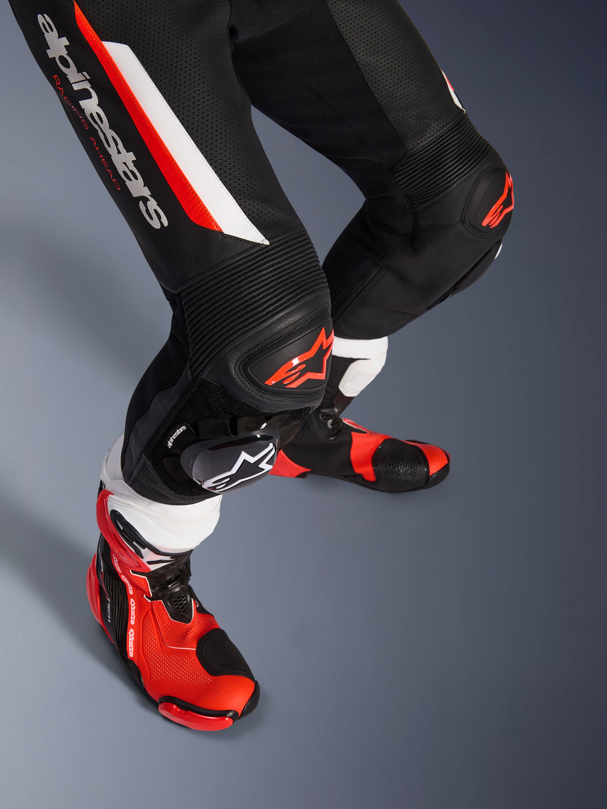 Alpinestars GP Force V2 1-Teiler Lederkombi, Schwarz, Weiß und Fluo-Rot, Nahaufnahme der Unterschenkel und Knie mit DFS Lite Protektoren und austauschbaren Knieschleifern, kombiniert mit professionellen Rennstiefeln