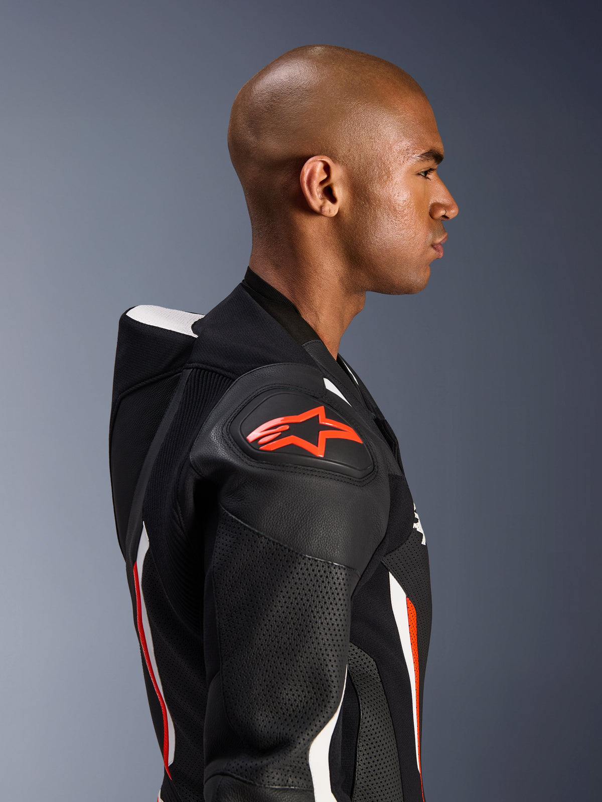 Alpinestars GP Force V2 Lederkombi – 1-Teiler, Seitenprofil eines Fahrers, Farbvariante Schwarz Weiß Rot Fluo, hebt den aerodynamischen Geschwindigkeitsbuckel, perforierte Lederzonen und den DFS Lite Schulterschutz mit rotem Alpinestars-Logo hervor