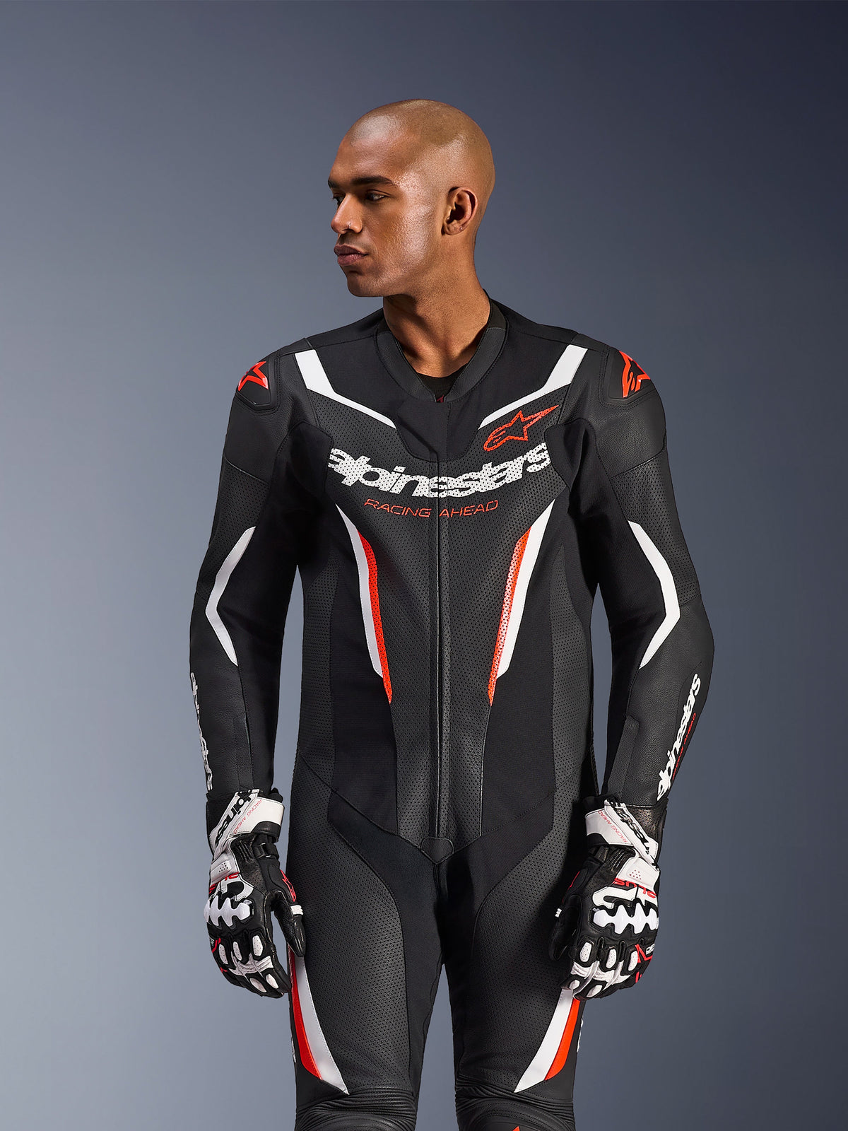 Alpinestars GP Force V2 Lederkombi 1-teilig, Schwarz Weiß Rot Fluo, getragen von einem männlichen Model mit Rennsport-Handschuhen, perforierte Lederkonstruktion, markante weiße und rote Grafikakzente, Alpinestars-Branding auf der Brust.