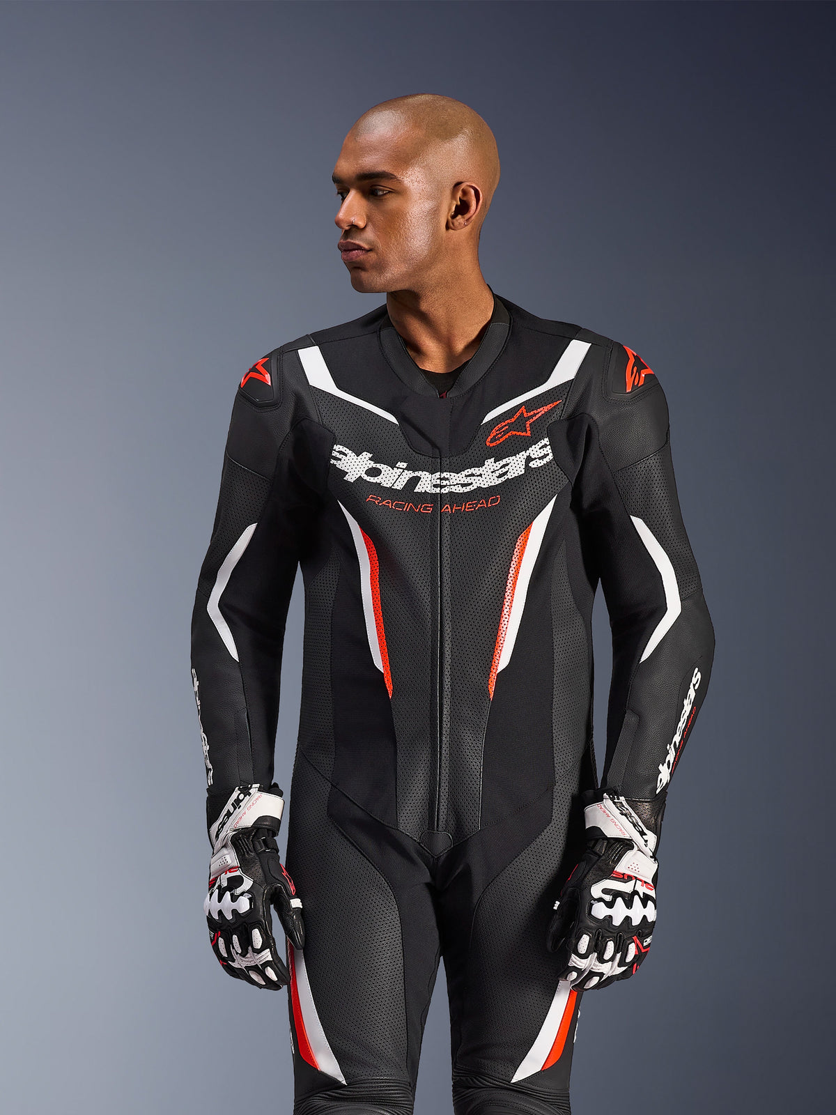 Alpinestars GP Force V2 Lederkombi – 1-Teiler, Motorrad-Rennanzug, Schwarz, Weiß und Rot Fluo, mit perforierten Lederpaneelen, markantem Branding auf der Brust mit dem Text „Racing Ahead“ und ergonomischem Schutzdesign, getragen mit passenden Rennhandschuhen