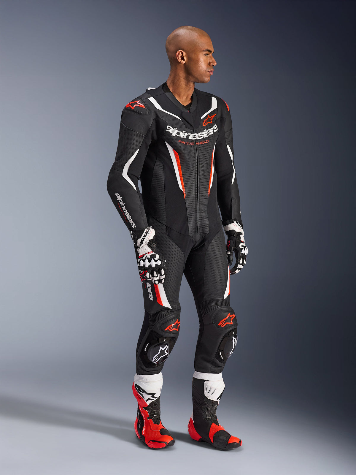 Model trägt die Alpinestars GP Force V2 Lederkombi 1-teilig in Schwarz Weiß Rot Fluo, Hochleistungs-Rennausrüstung mit perforierten Lederpanelen und DFS Lite Schilden, kombiniert mit passenden rot-weißen Rennstiefeln und Handschuhen, professionelle Motorsport-Ästhetik.