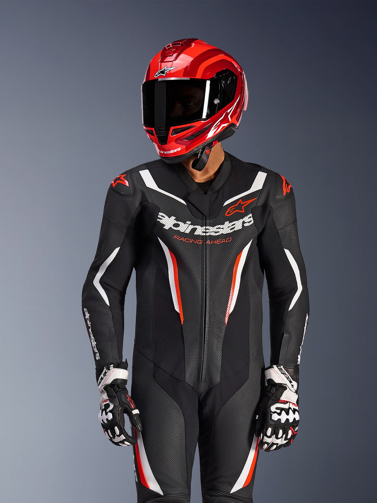 Motorradfahrer in Alpinestars GP Force V2 1-Teiler Lederkombi in Schwarz Weiß Rot Fluo, dazu passender roter Rennhelm und Handschuhe, mit perforierten Lederpaneelen und markantem Branding, Hochleistungs-Rennausrüstung