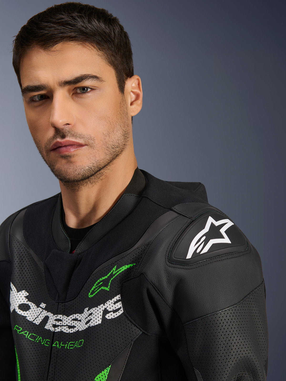 Alpinestars GP Force V2 Leather Suit - 1Piece, Black and Green, close-up of a male model wearing the motorcycle racing suit, featuring white and green logo branding, perforated leather panels, and DFS Lite shoulder armor with a white star logo.