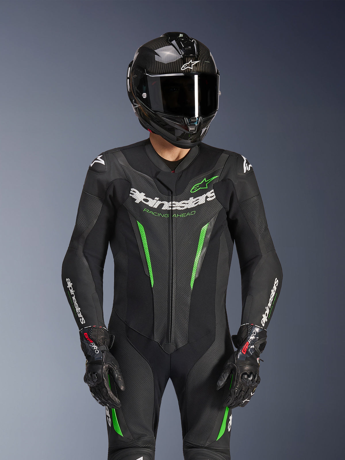Alpinestars GP Force V2 Leather Suit - 1Piece, Black and Green, motorcycle racing suit worn with a carbon fiber helmet and GP Pro gloves, featuring lime green accents and Alpinestars 'Racing Ahead' branding, engineered for track performance.