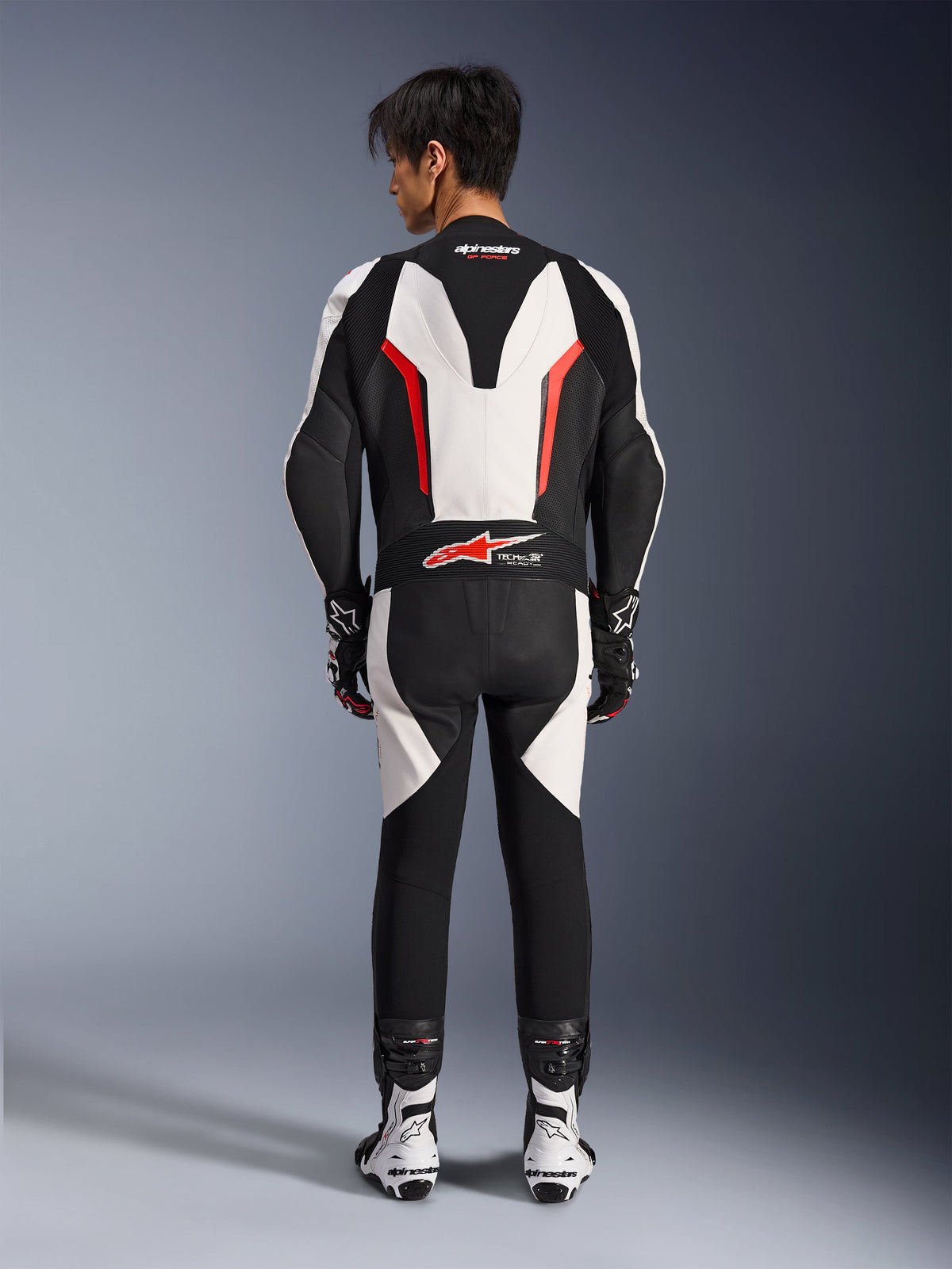 Alpinestars GP Force V2 Lederkombi 1-teilig, Motorrad-Rennkombi, Weiß Schwarz und Red Fluo, Rückansicht eines Modells mit Rennstiefeln und Handschuhen, mit aerodynamischem Geschwindigkeitsbuckel, Akkordeon-Stretch-Einsätzen und Tech-Air Ready-Branding