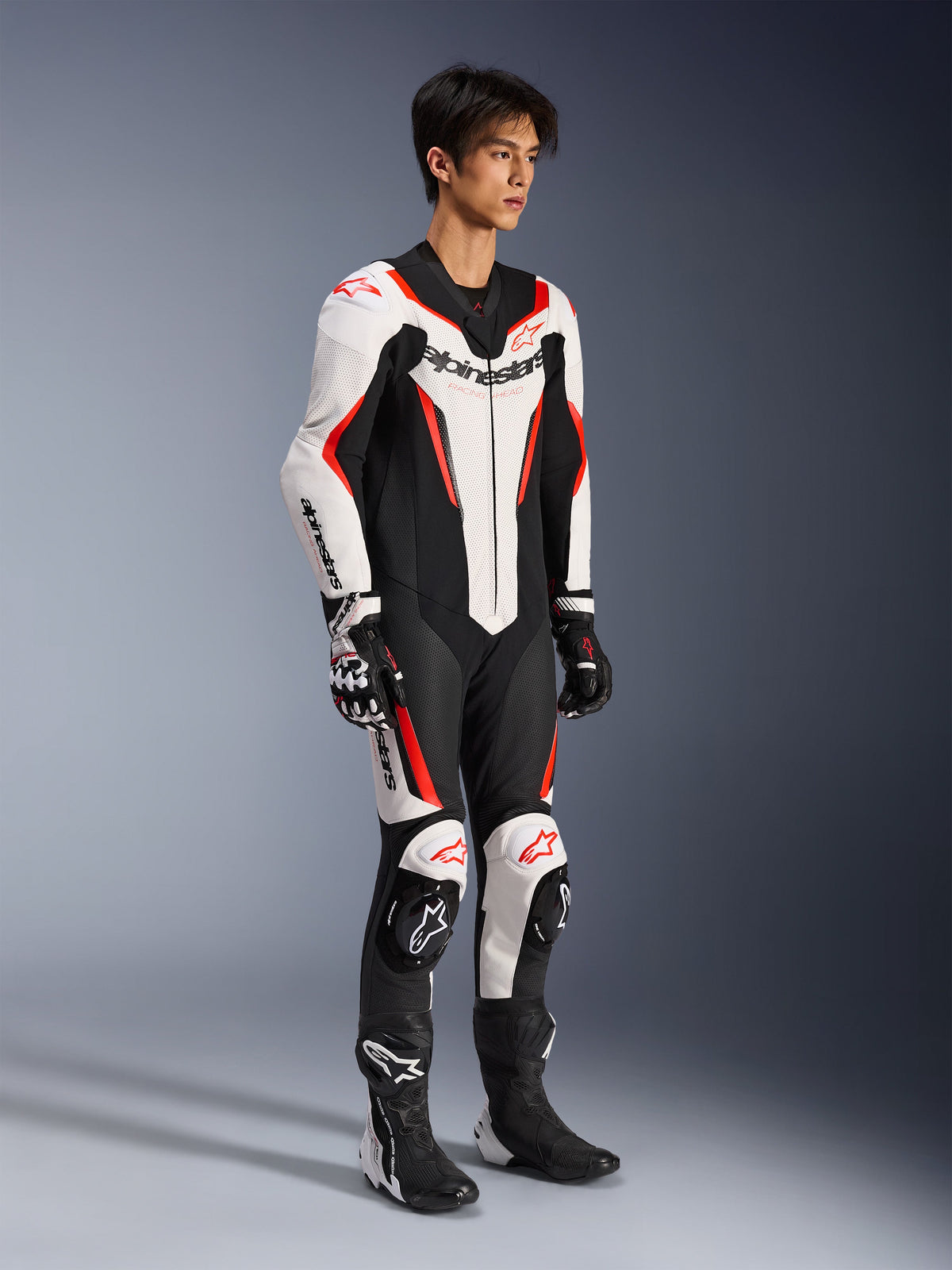 Alpinestars GP Force V2 Lederkombi – 1-Teiler, einteiliger Motorrad-Rennanzug, Weiß, Schwarz und Rot Fluo, getragen mit passenden Handschuhen und Stiefeln, mit perforiertem Leder und markantem Alpinestars-Branding, aerodynamisches Design für Performance auf der Rennstrecke