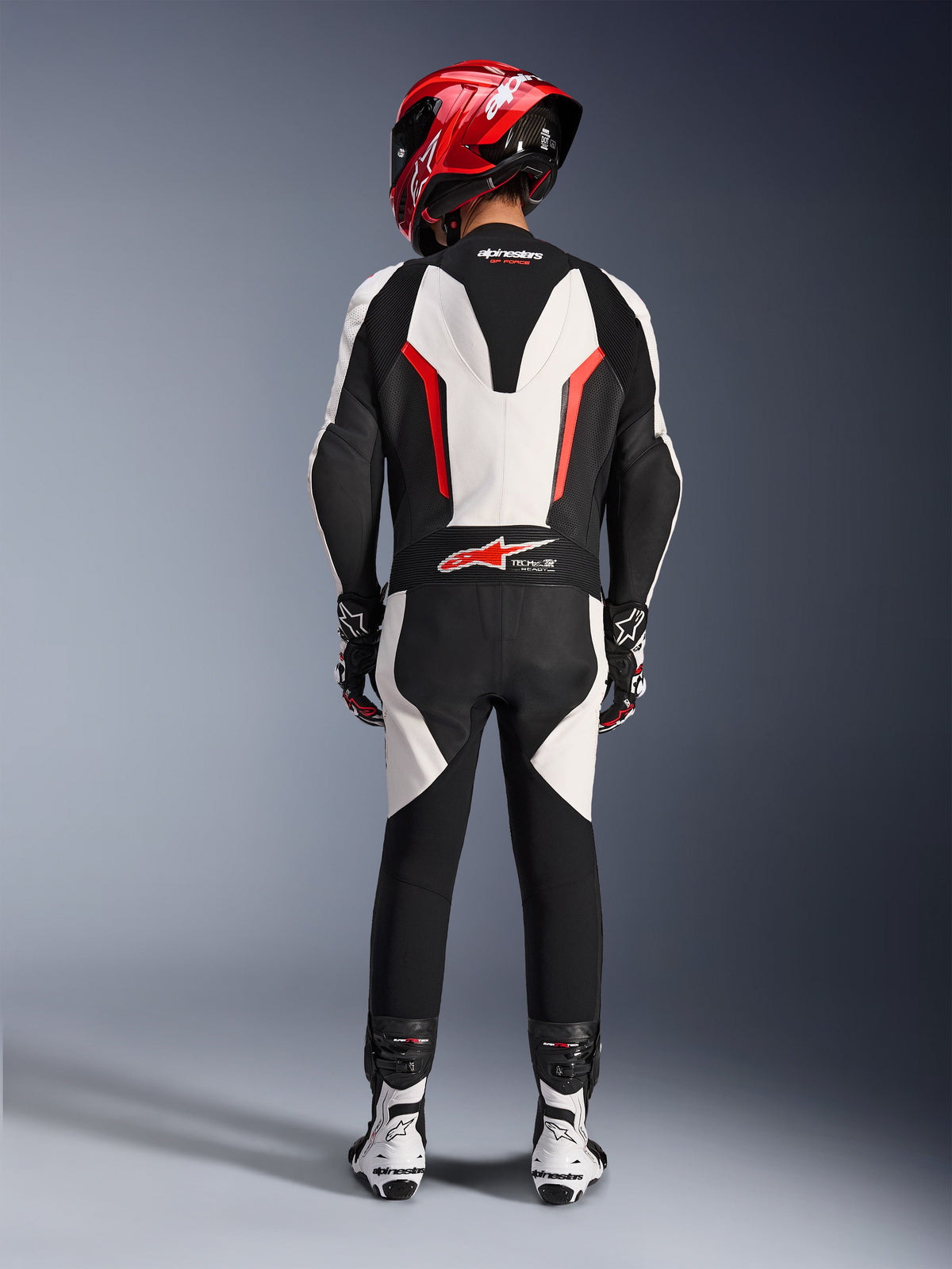 Alpinestars GP Force V2 Lederkombi - 1-teilig, Weiß Schwarz Rot Fluo, Rückansicht mit Fokus auf den aerodynamischen Geschwindigkeitsbuckel und das Tech-Air Ready-Branding, getragen mit rotem Rennhelm und weiß-schwarzen Stiefeln, rennstreckenorientierte Lederkombi für Performance-Fahrten.