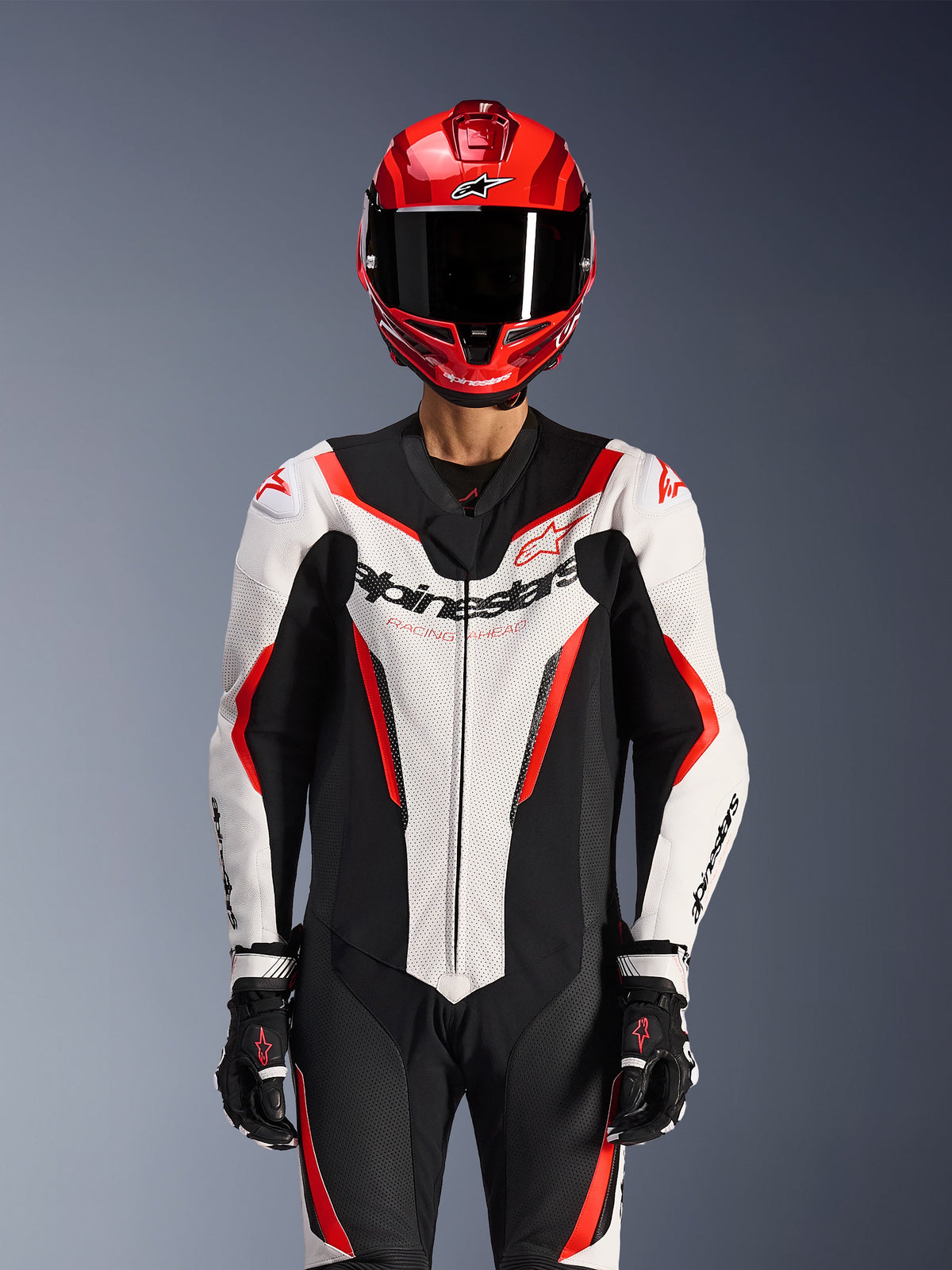 Alpinestars GP Force V2 Lederkombi - 1-teilig, Weiß Schwarz Rot Fluo, getragen mit rotem Integralhelm und schwarzen Rennhandschuhen, mit perforierten Lederbahnen und markantem Alpinestars-Branding auf der Brust, professionelle Performance-Ausrüstung für Motorradrennen