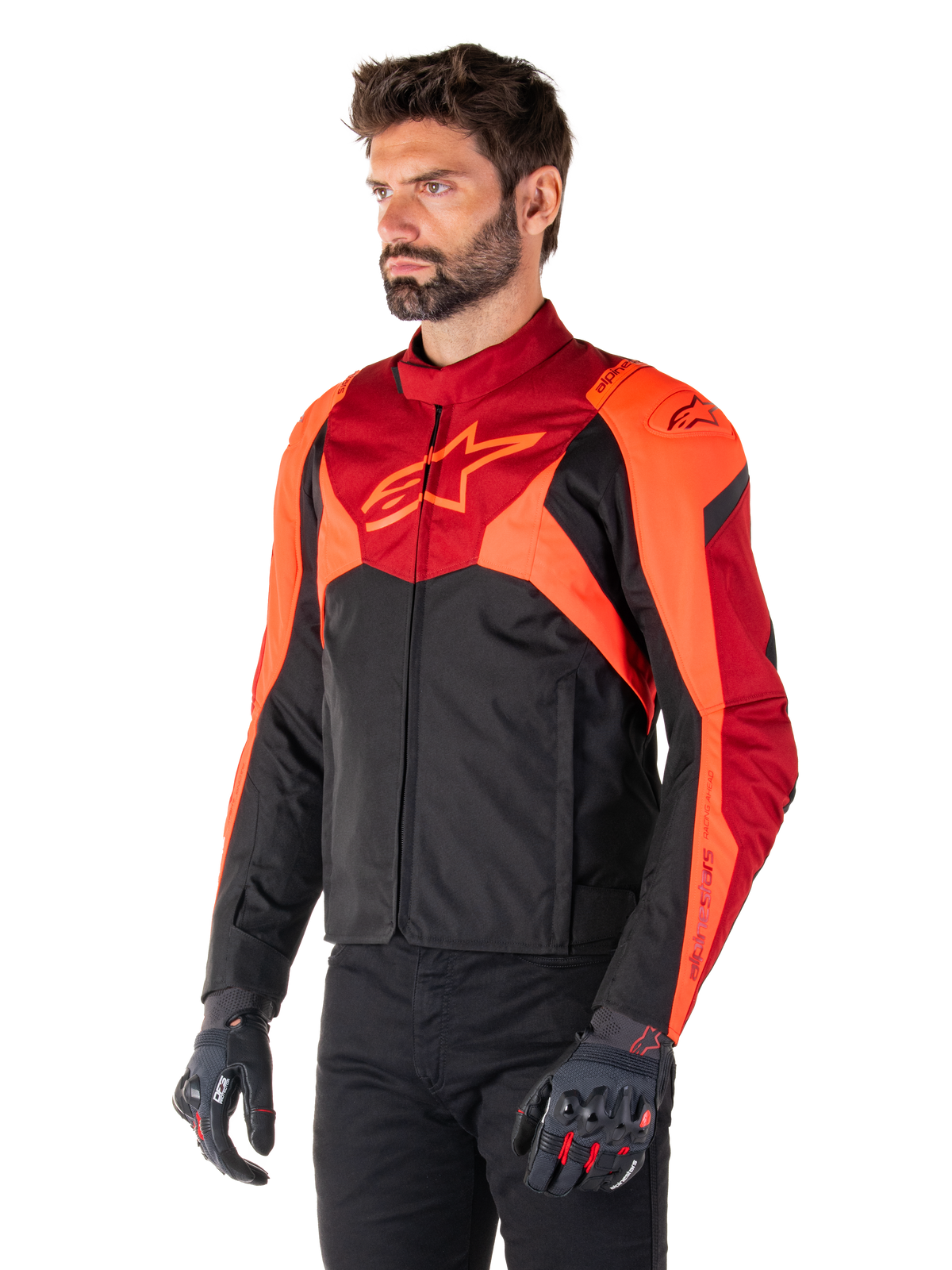 Alpinestars T-Jaws V4 Wasserdichte Jacke, Schwarz, Rot Fluo und Dunkelrot, getragen von einem männlichen Model mit schwarzer Hose und Motorradhandschuhen, aggressive sportliche Silhouette mit Alpinestars-Logo auf der Brust, Dreiviertelansicht