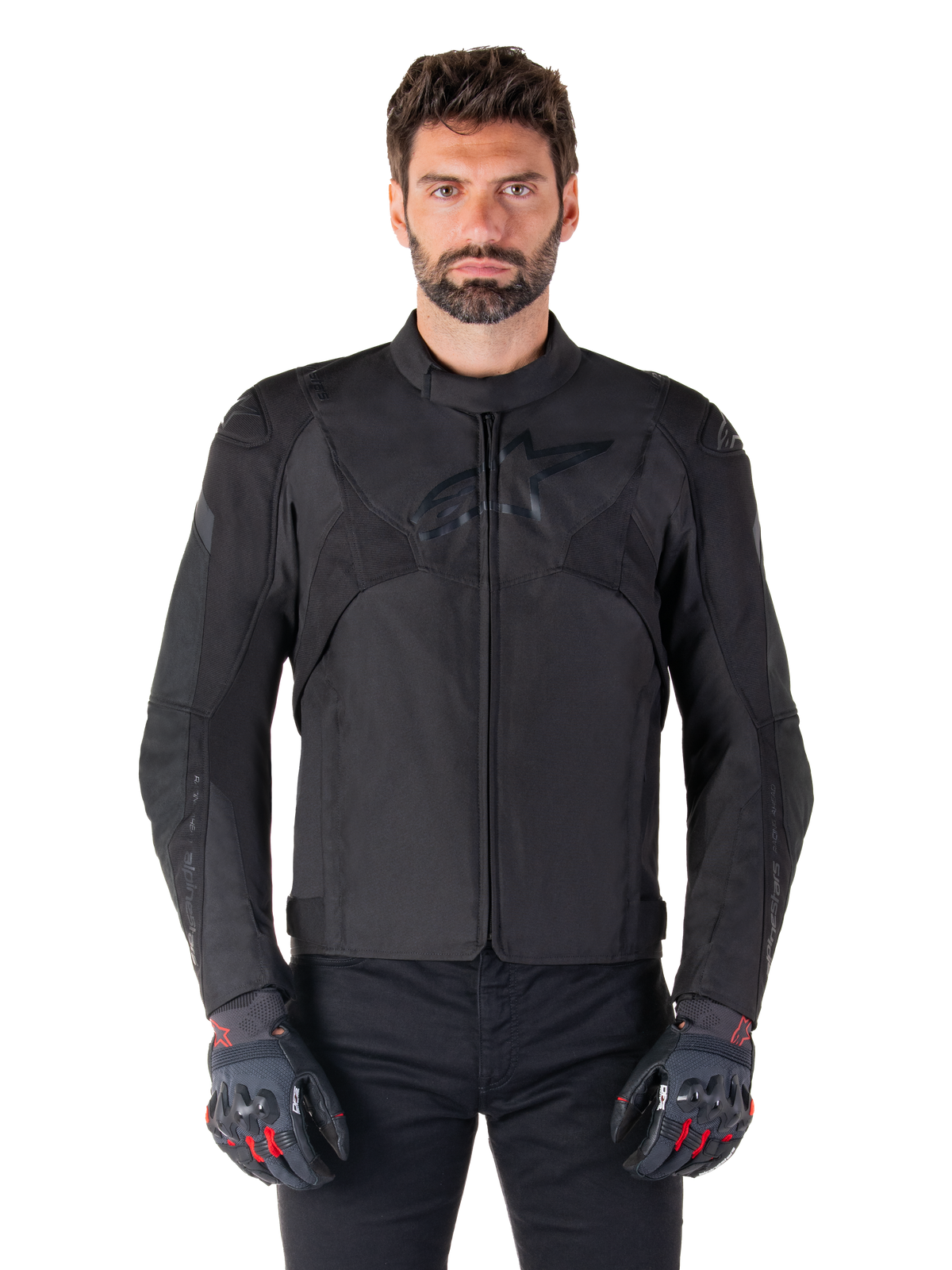 Alpinestars T-Jaws V4 Wasserdichte Jacke, schwarze Motorrad-Sportjacke, getragen von einem Mann mit schwarzen Handschuhen mit roten Akzenten, verstärkte Schultern und Arme, elegantes Design mit dezentem Brustlogo, textile Allwetter-Fahrerausrüstung