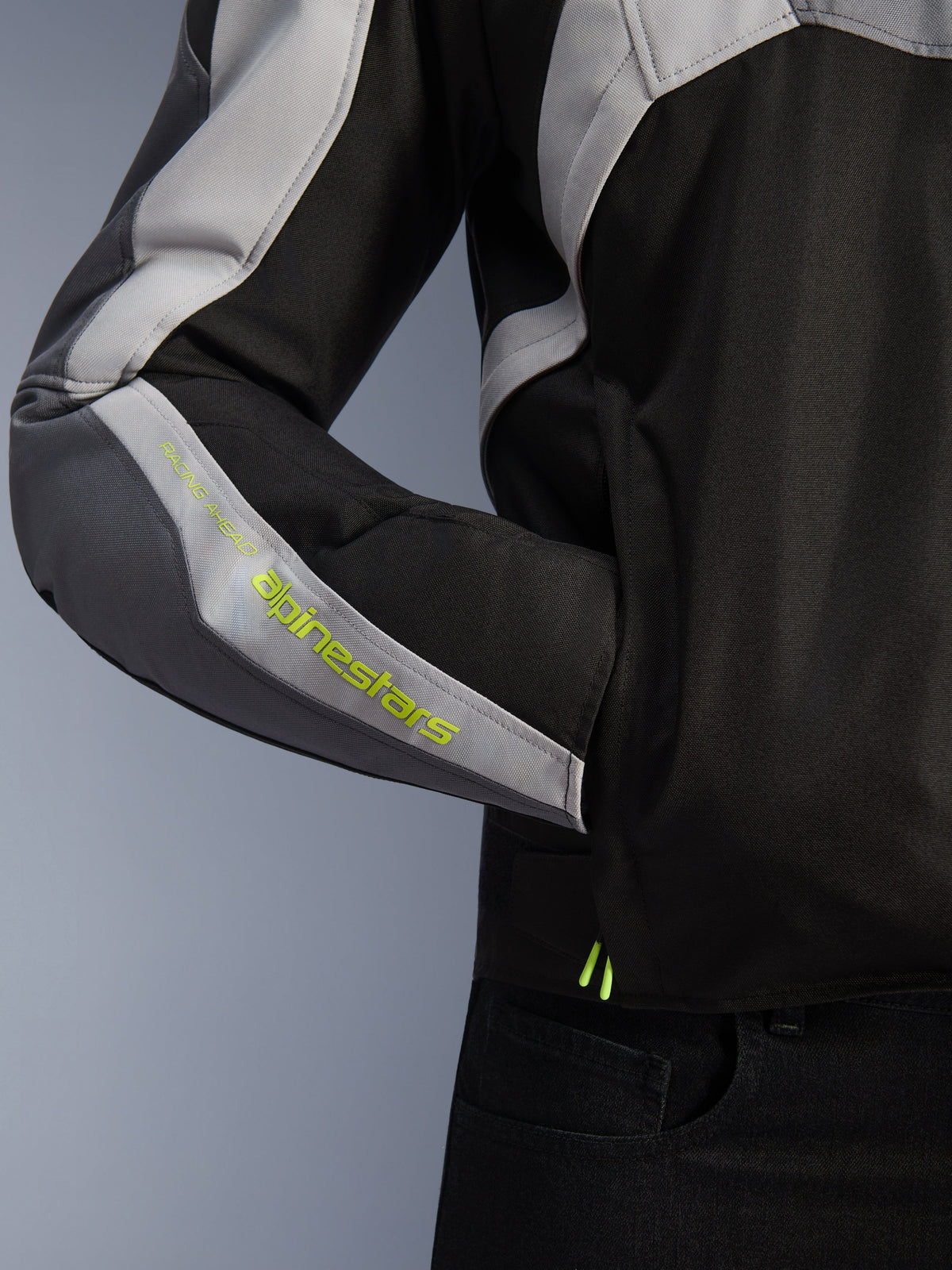 Alpinestars T-Jaws V4 Wasserdichte Jacke, Motorradjacke, Schwarz, Eisgrau und Dunkelgrau, Nahaufnahme des Ärmels mit neongelbem Alpinestars-Branding, Textilmaterial mit Seitentasche und Multi-Panel-Design.