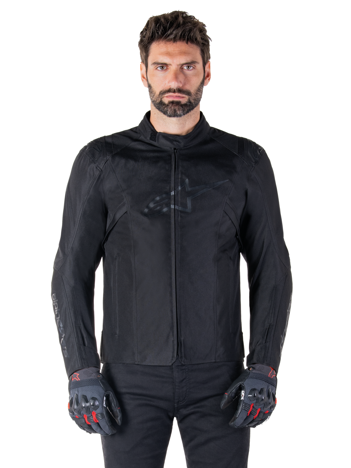 Alpinestars T-SPS V2 Waterproof Jacket, schwarze Motorrad-Textiljacke, getragen von einem Fahrer mit schwarz-roten Handschuhen, hoher Kragen, Reißverschluss vorne, dezentes Brustlogo, wasserdichter Schutz für sportliches und urbanes Fahren