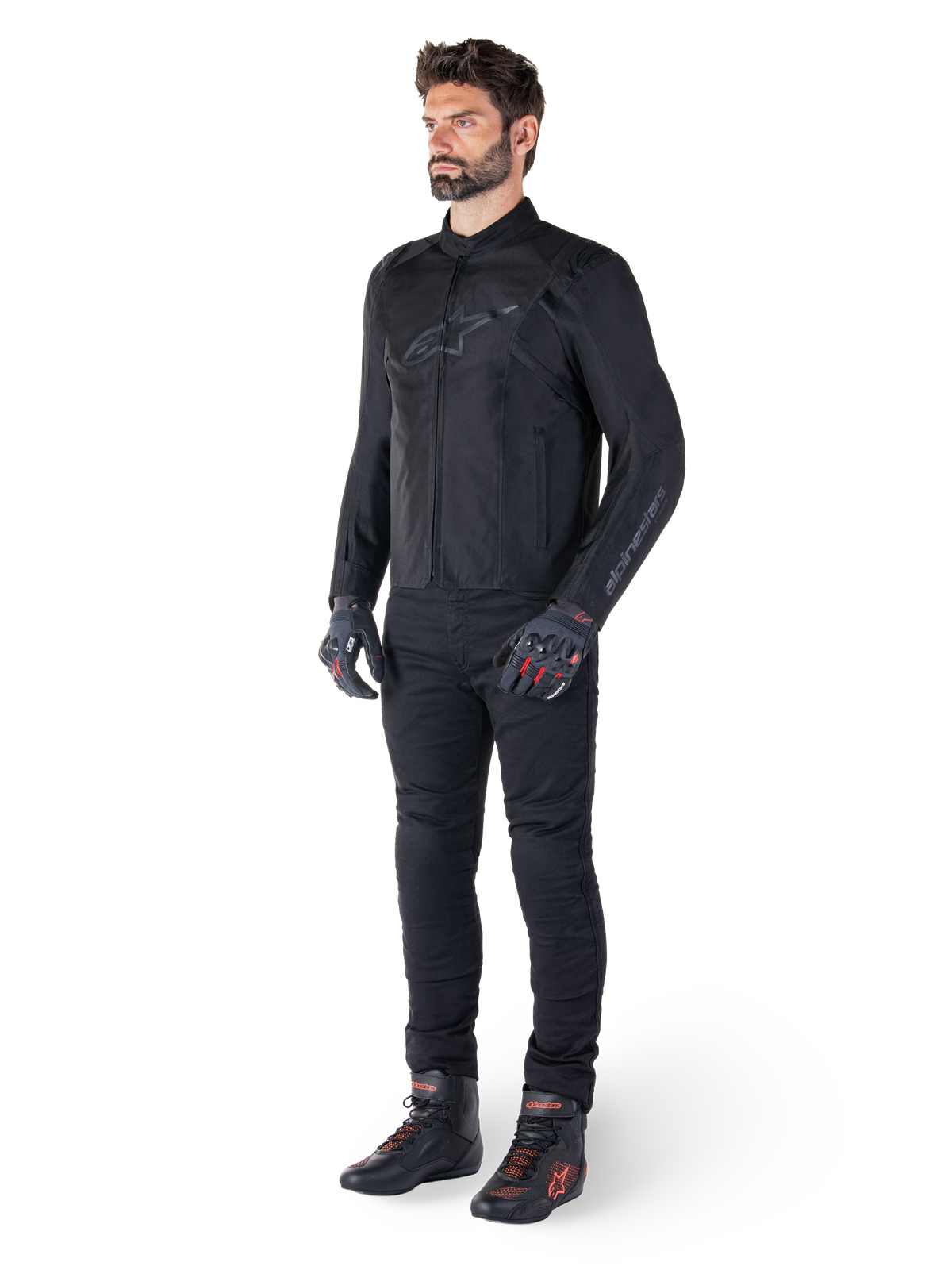 Alpinestars T-SPS V2 Waterproof Jacke, Schwarz, getragen von einem männlichen Model mit passender schwarzer Hose, schwarzen Handschuhen mit roten Akzenten und schwarzen Motorradschuhen, komplette Motorradausrüstung für Urban- und Sport-Fahrten, sauberer weißer Hintergrund