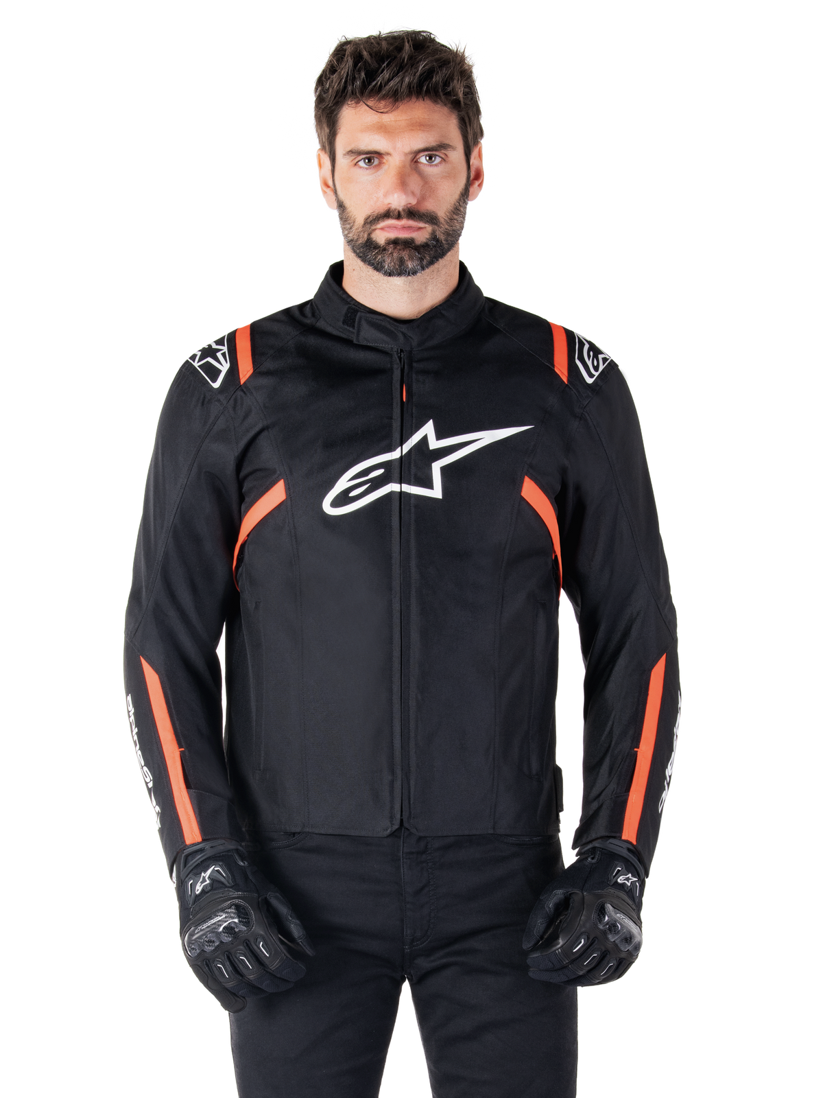 Alpinestars T-SPS V2 Waterproof Jacket, Black White and Red Fluo, worn by a male model with black riding gloves, featuring a large white Alpinestars logo on the chest and vibrant orange accents on the shoulders and sleeves.