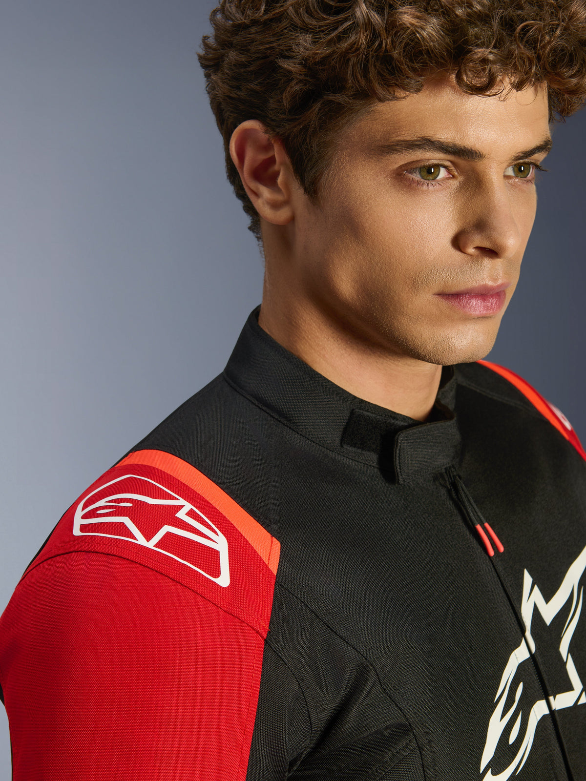 Alpinestars T-SPS V2 Waterproof Jacket, motorcycle textile jacket, Black Red and Red Fluo, close-up shot of model wearing the jacket, featuring prominent white Alpinestars logos on shoulder and chest, low-profile collar, and athletic sport fit.