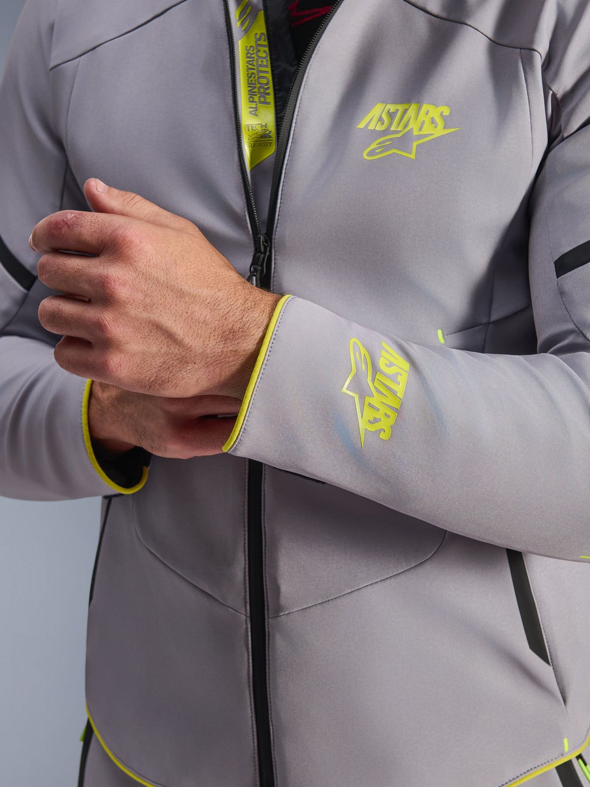 Alpinestars Aeroshell Waterproof Jacket, Mid Gray with Yellow Fluo accents, close-up of chest and sleeve cuff showing fluorescent yellow Astars logos, detail of internal flap with Tech-Air Ready branding, modern sports softshell motorcycle jacket