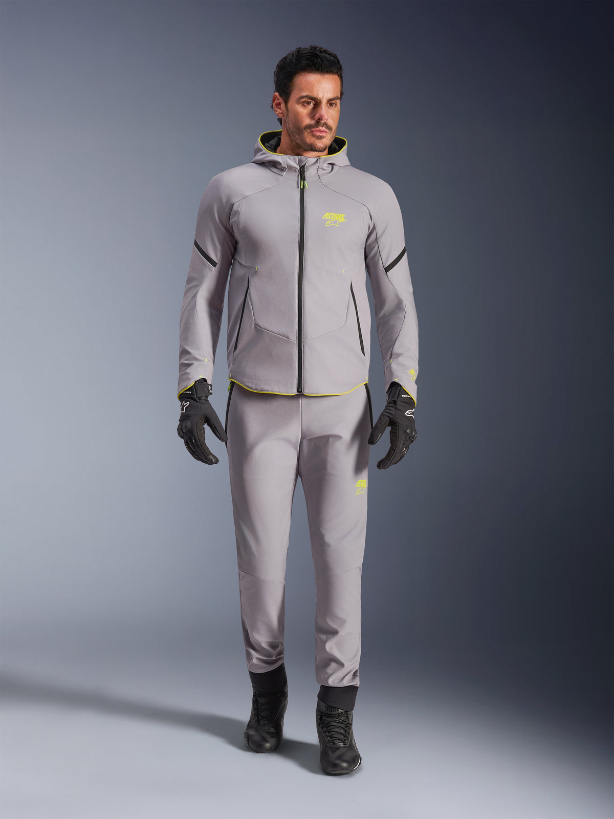 Alpinestars Aeroshell Waterproof Jacket, Mid Gray Yellow Fluo, worn with matching gray pants, black gloves and boots, featuring a modern sport-inspired hoodie design with vibrant yellow accents and athletic fit.