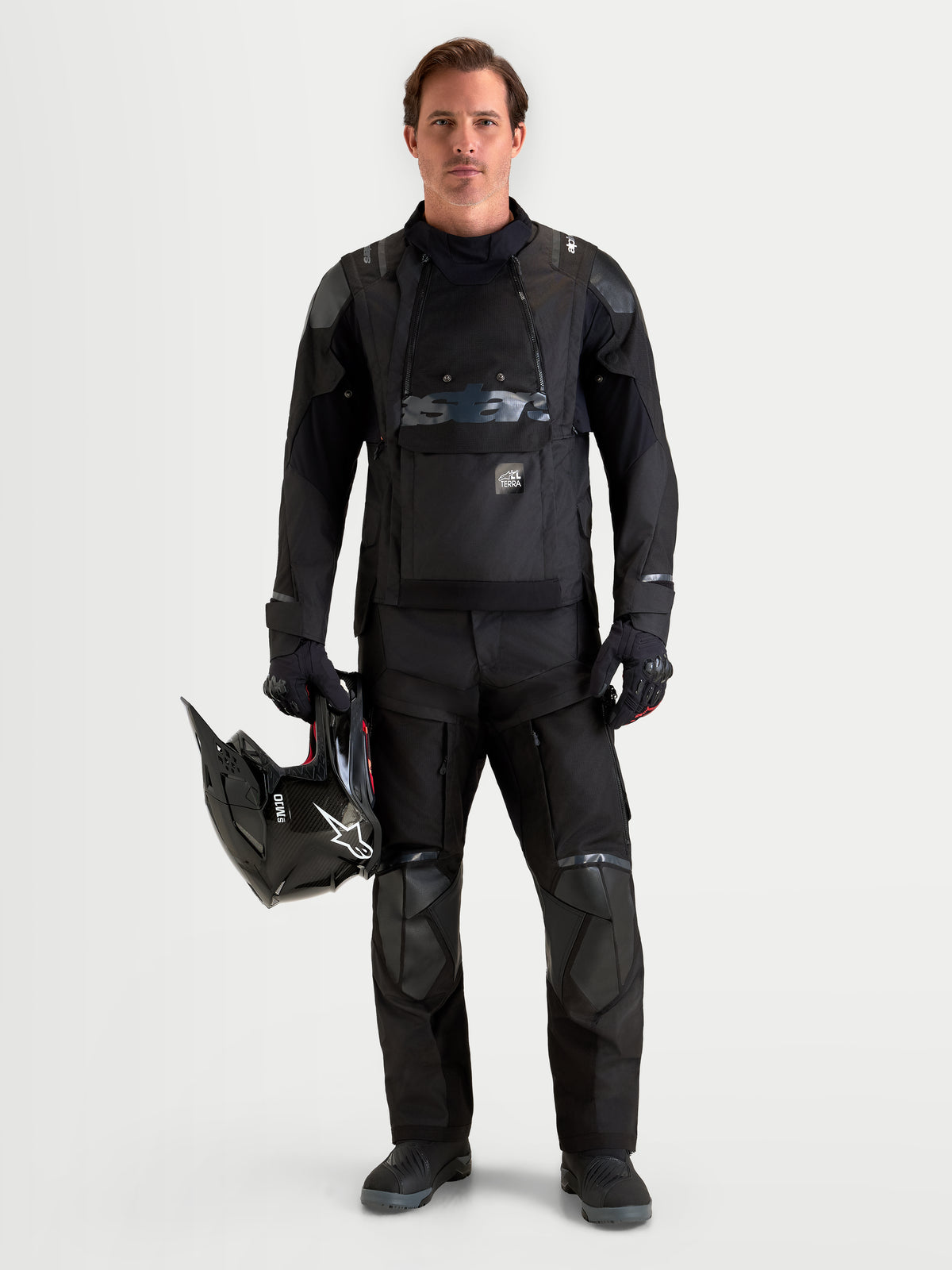 Alpinestars Harok V2 Drystar Jacket, Men's Black adventure motorcycle jacket worn with matching riding pants and holding a helmet, featuring waterproof textile construction and modular ventilation