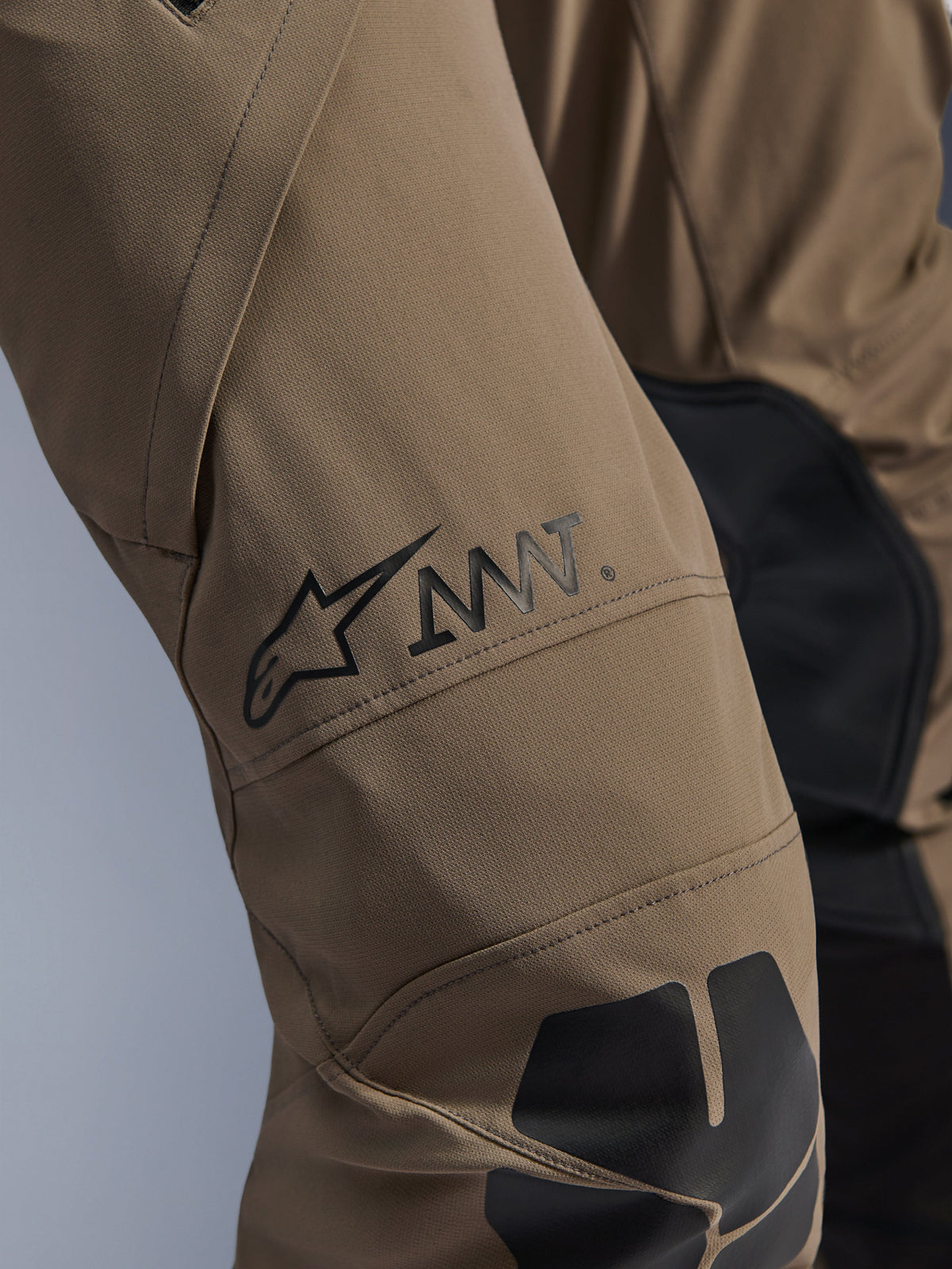 Alpinestars AMT-8 Stretch Drystar® XF Pants in Walnut Black, close-up of the leg featuring the black AMT logo and Alpinestars star, high-performance stretch textile with black panels, technical adventure motorcycle gear