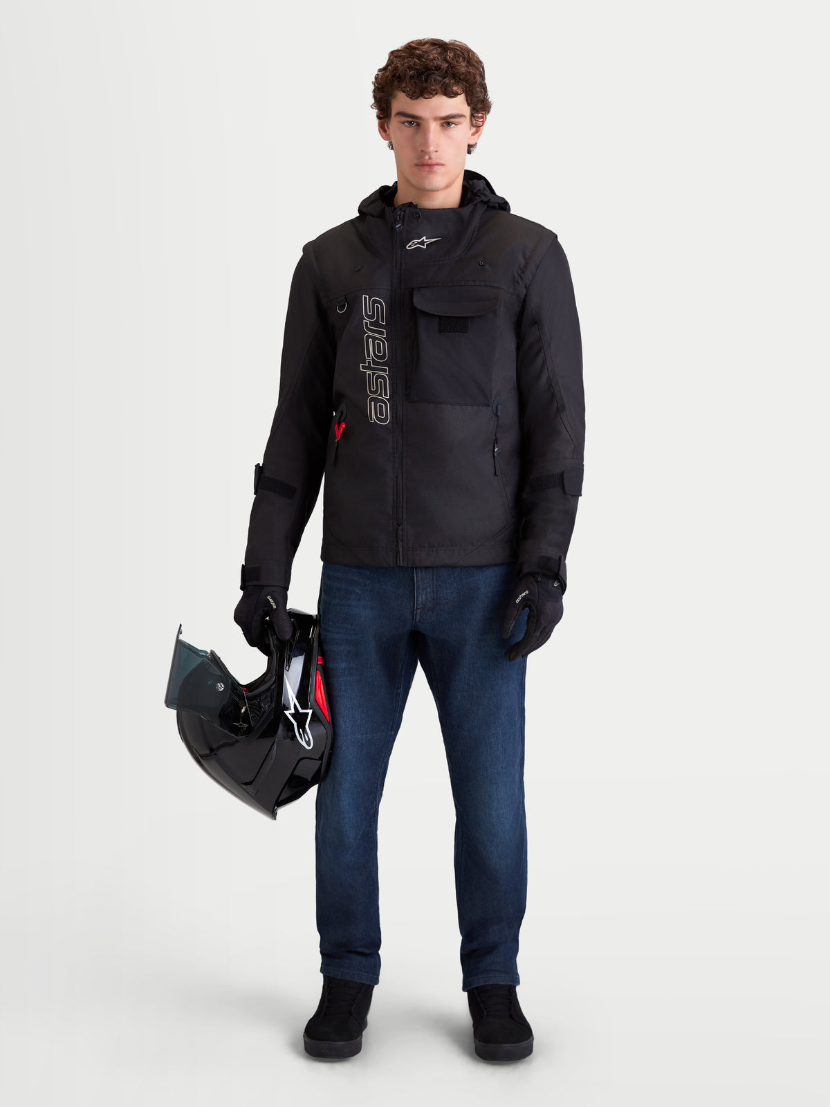 Alpinestars Morfex Parka Jacke, urbane Herren-Motorradjacke in Schwarz, Frontansicht an einem Model mit Jeans und Helm, mit modularem Design und integrierter Kapuze