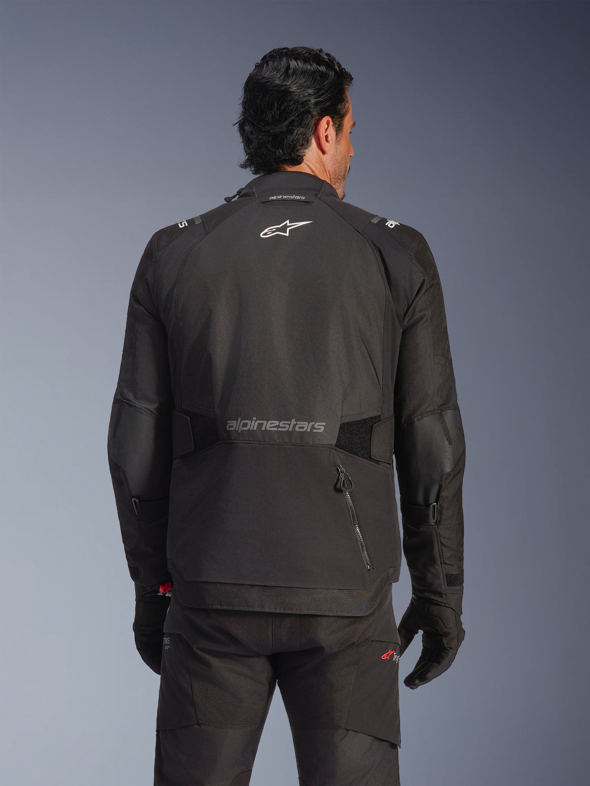 Alpinestars Andes V4 Drystar® Jacke, Schwarz, Rückansicht an einem Model, Textil-Adventure-Jacke mit reflektierenden Logos und einer Rückentasche mit Reißverschluss, kombiniert mit passender schwarzer Hose und Handschuhen